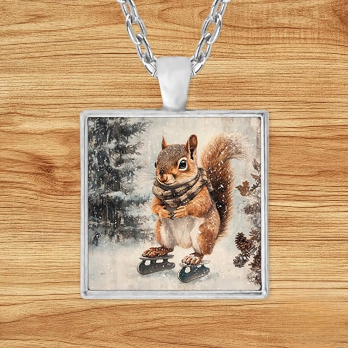 Square silver charm pendant necklace featuring a plaid-scarf squirrel ice skating across a frozen pond in a snowy pine forest