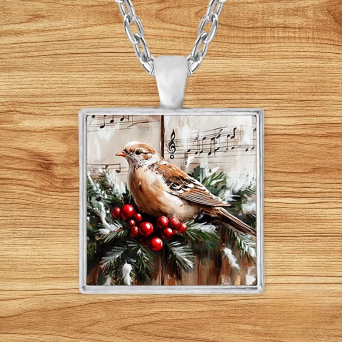 Square silver charm pendant necklace featuring a white dove perched on a pine branch with red berries over vintage sheet music