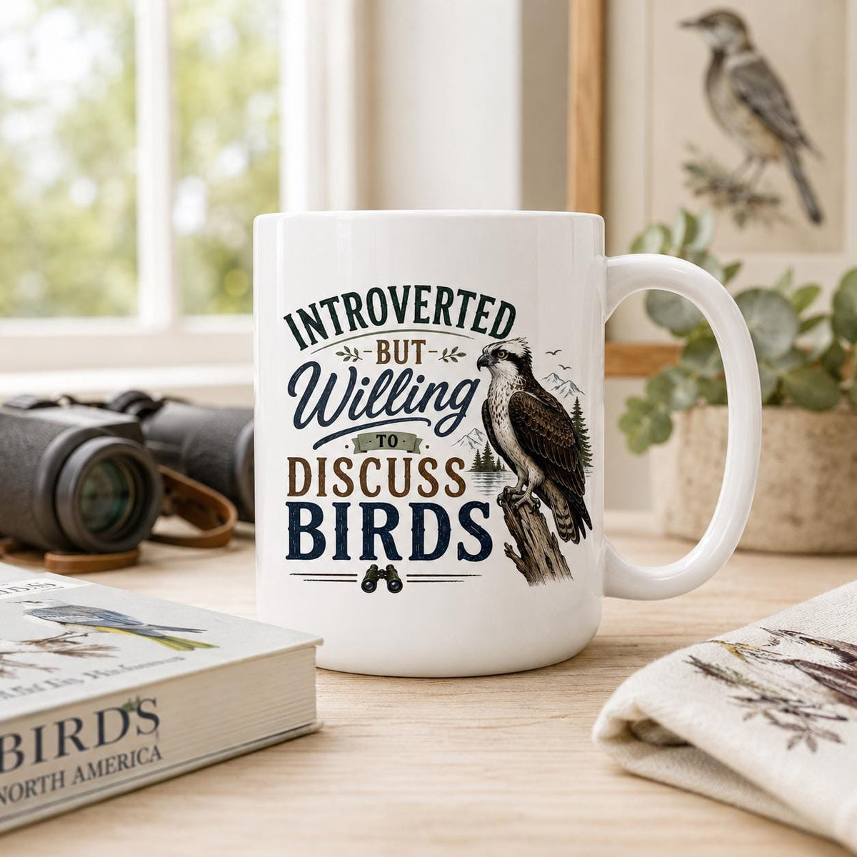 Introverted birder osprey mug on a wooden desk with binoculars, a Birds of North America guide and a bird print