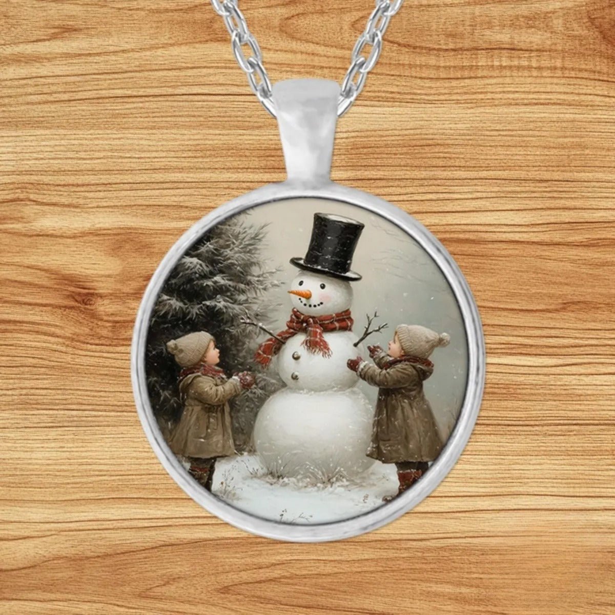 Round silver charm pendant necklace featuring two children in vintage knit hats building a top-hat snowman in a snowy evergreen forest
