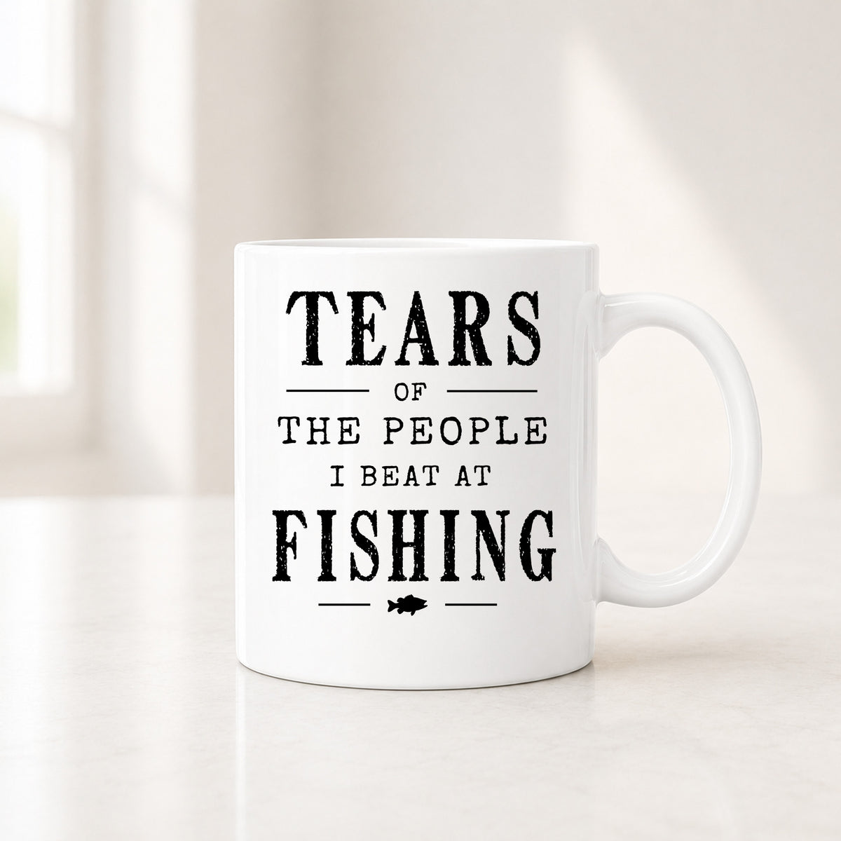 11 oz white fishing mug with the black Tears of the People I Beat quote, on a light counter by a window