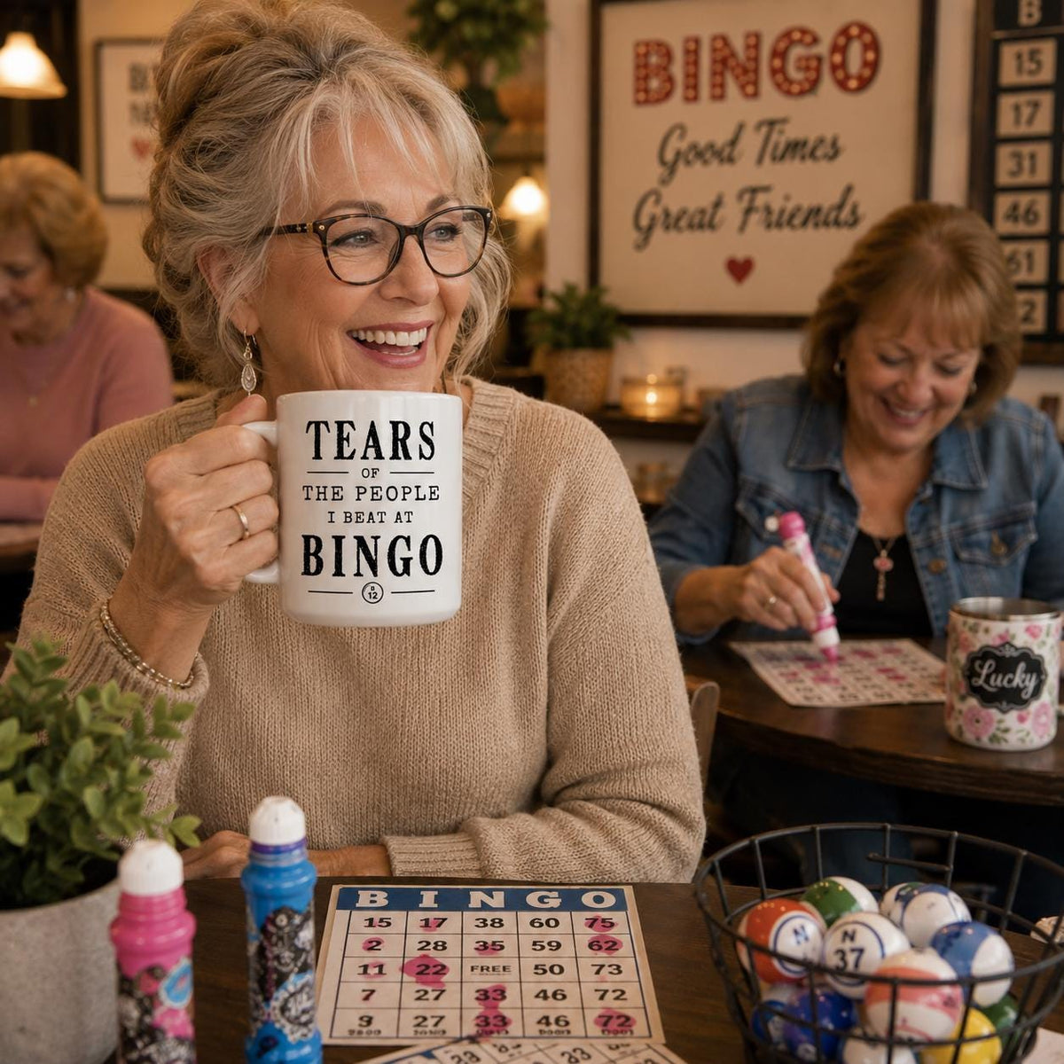 Smiling woman seated at a table holding the white Tears of the People I Beat at Bingo mug