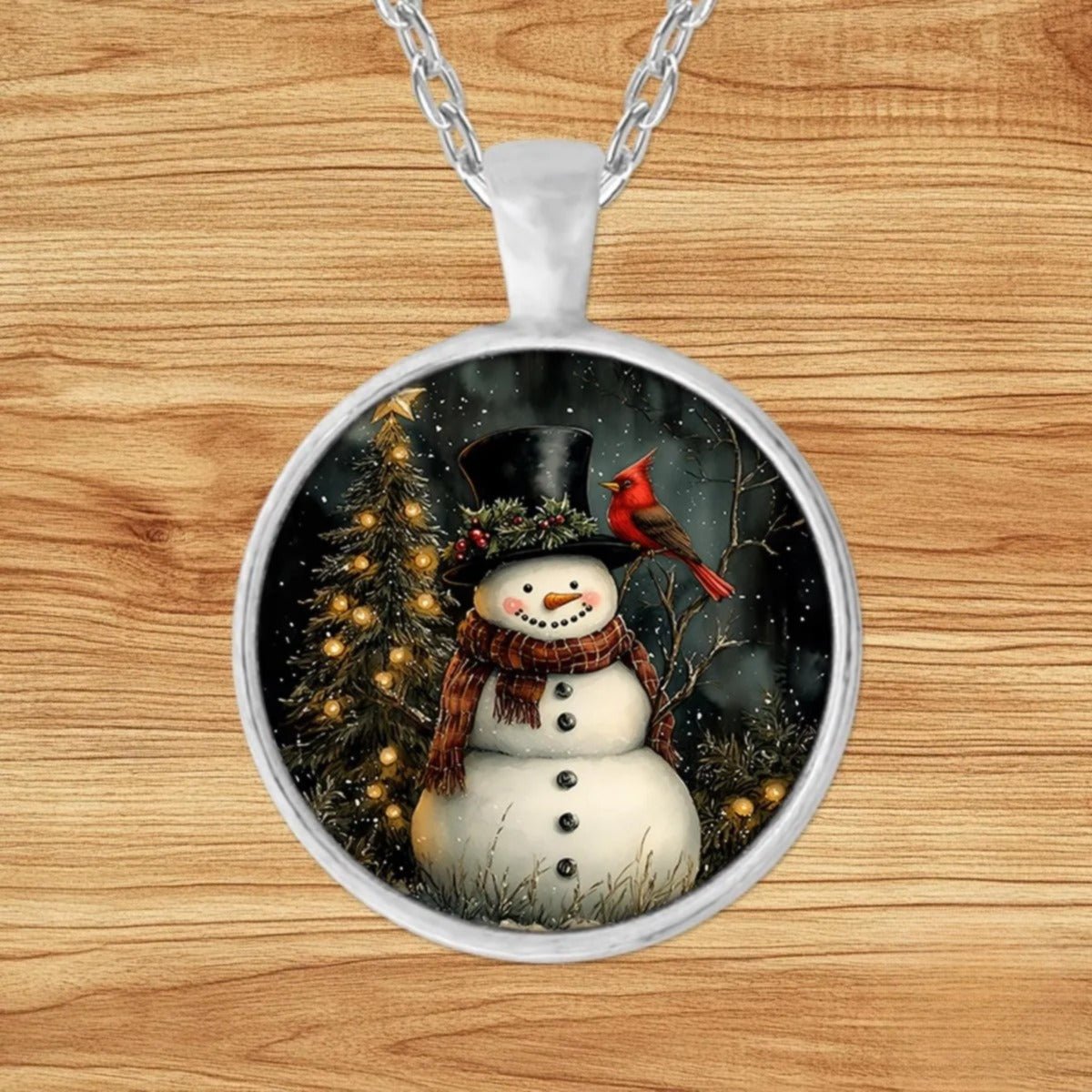 Round silver charm pendant necklace featuring a top-hat snowman in a red plaid scarf beside a red cardinal in a moonlit forest
