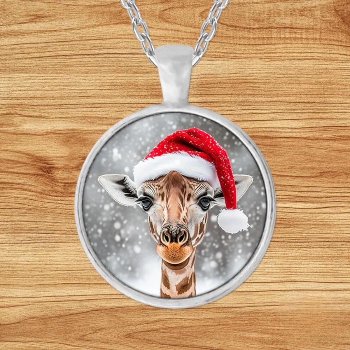 Round silver charm pendant necklace featuring a baby giraffe in a red Santa hat with white fur trim against a snowy background