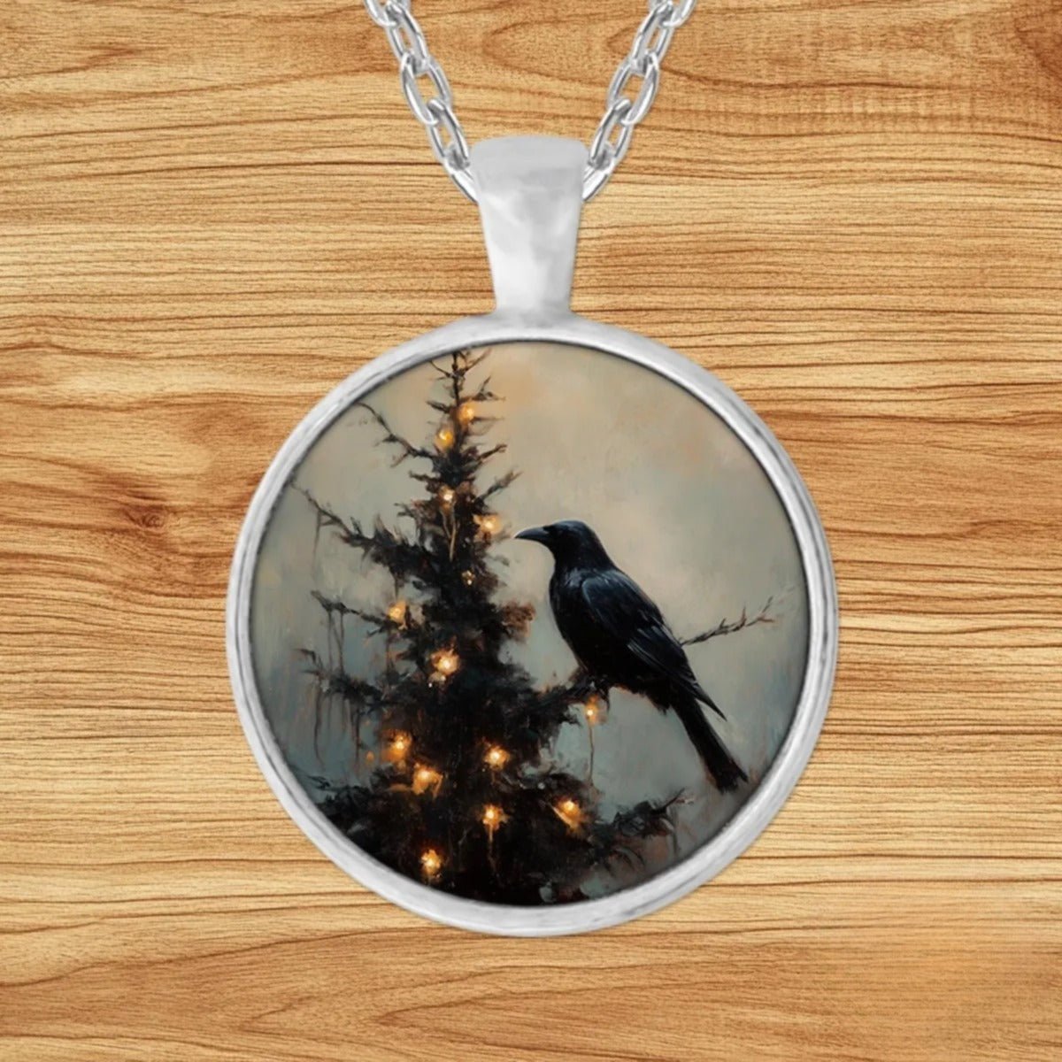 Round silver charm pendant necklace featuring a black raven perched on an evergreen tree dripping with golden candle-like lights