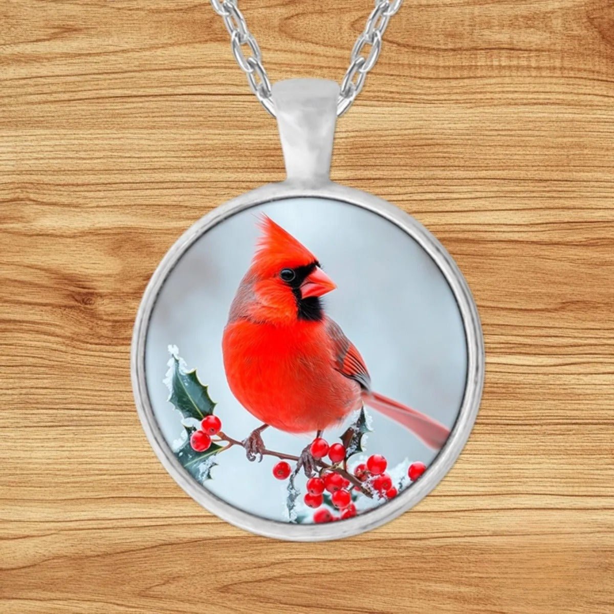 Round silver charm pendant necklace featuring a red cardinal perched on a snow-dusted branch with winter berries