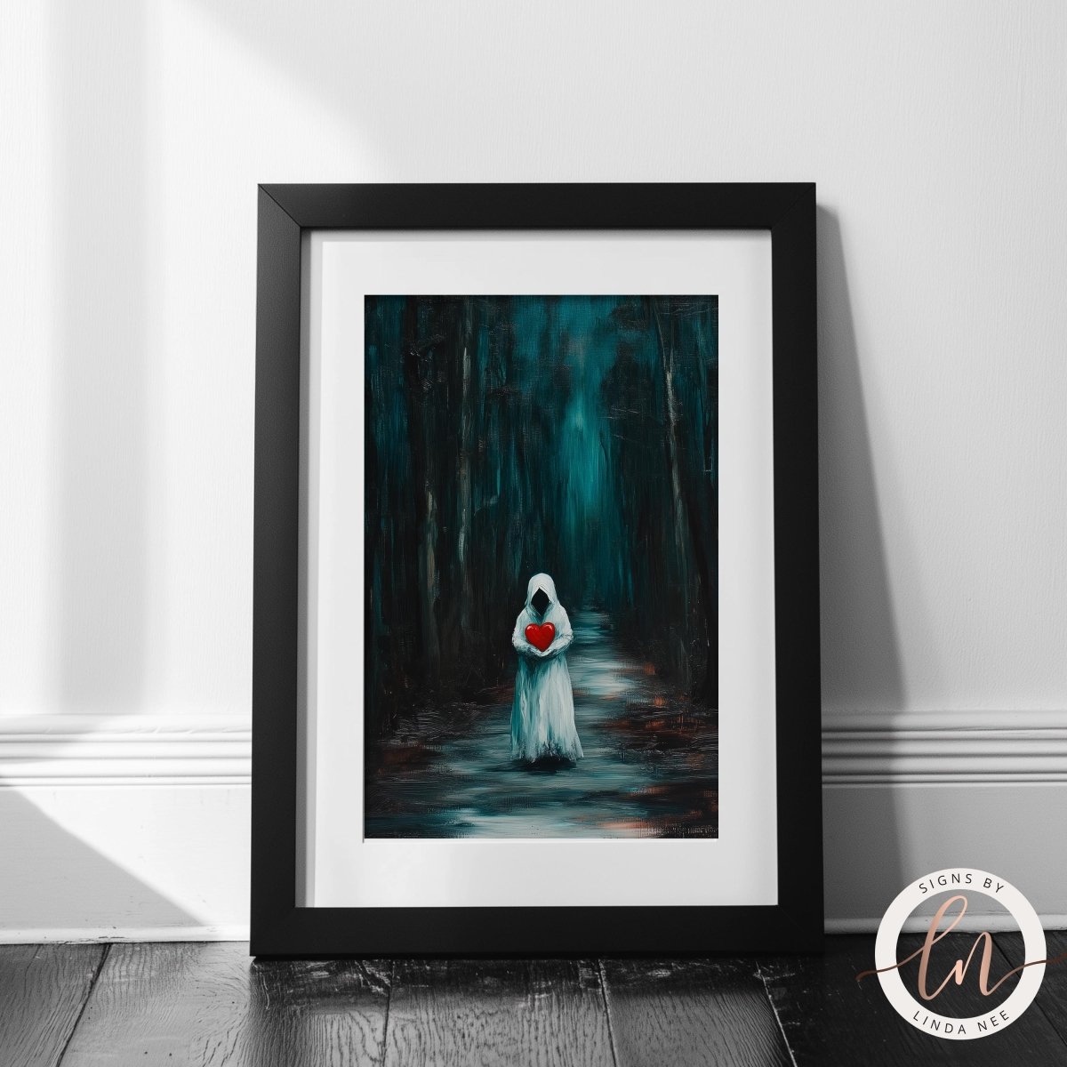 A framed art print leaning against a white wall on a dark wood floor. The print shows a ghostly white figure holding a glowing red heart in a dark teal forest.