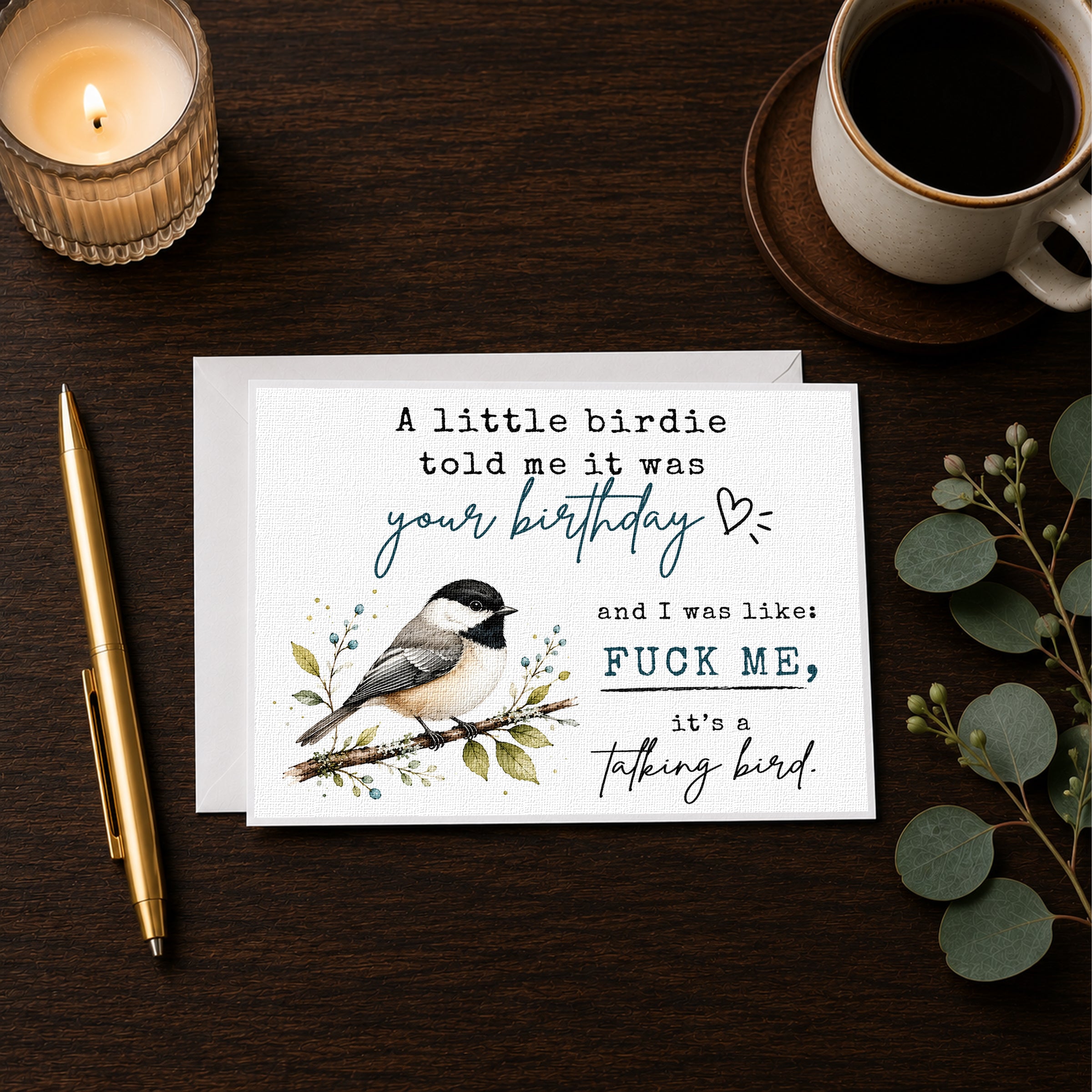 a birthday card with a humorous message, a candle, a pen, and a cup of coffee on a wooden surface.