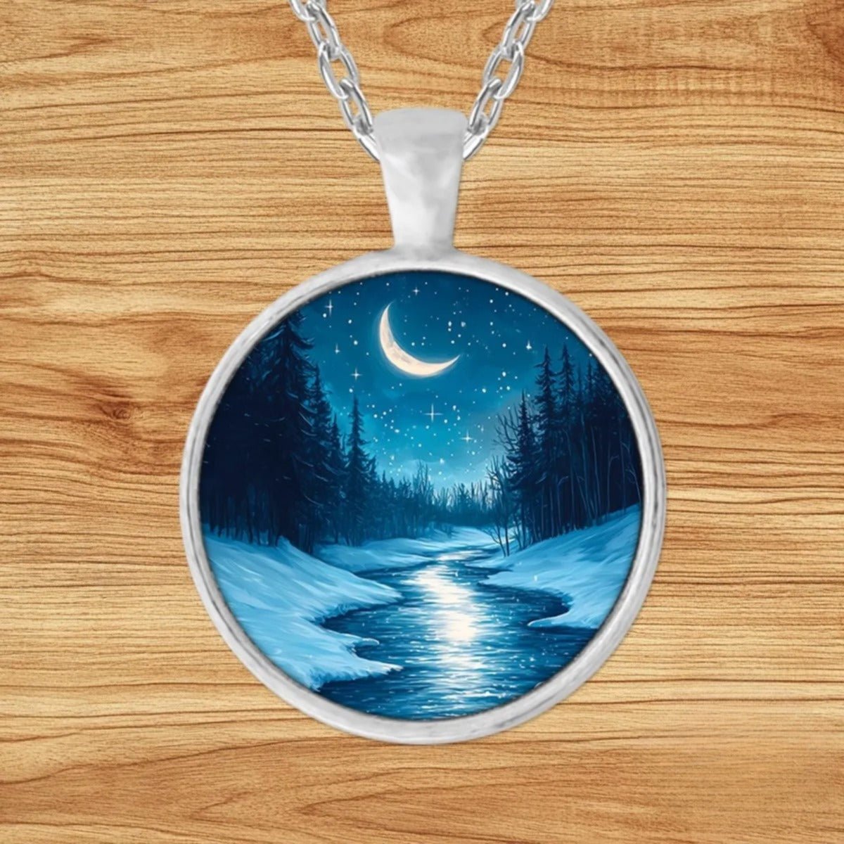 Round silver charm pendant necklace featuring a glowing crescent moon over a snowy pine forest with a frozen, moonlit stream
