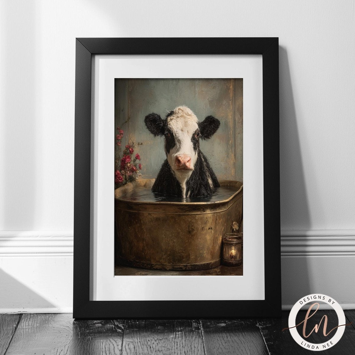 A framed photograph of a black and white cow sitting in a large metal tub filled with water, with a vase of flowers in the background.