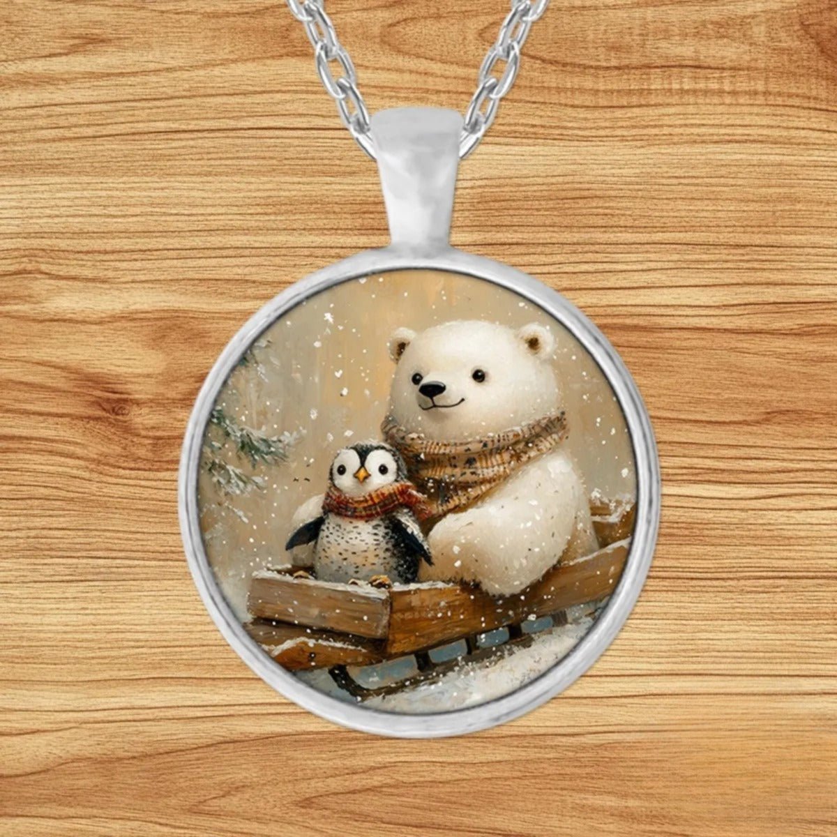 Round silver charm pendant necklace featuring a polar bear and penguin duo riding a wooden sled through a snowy evergreen forest