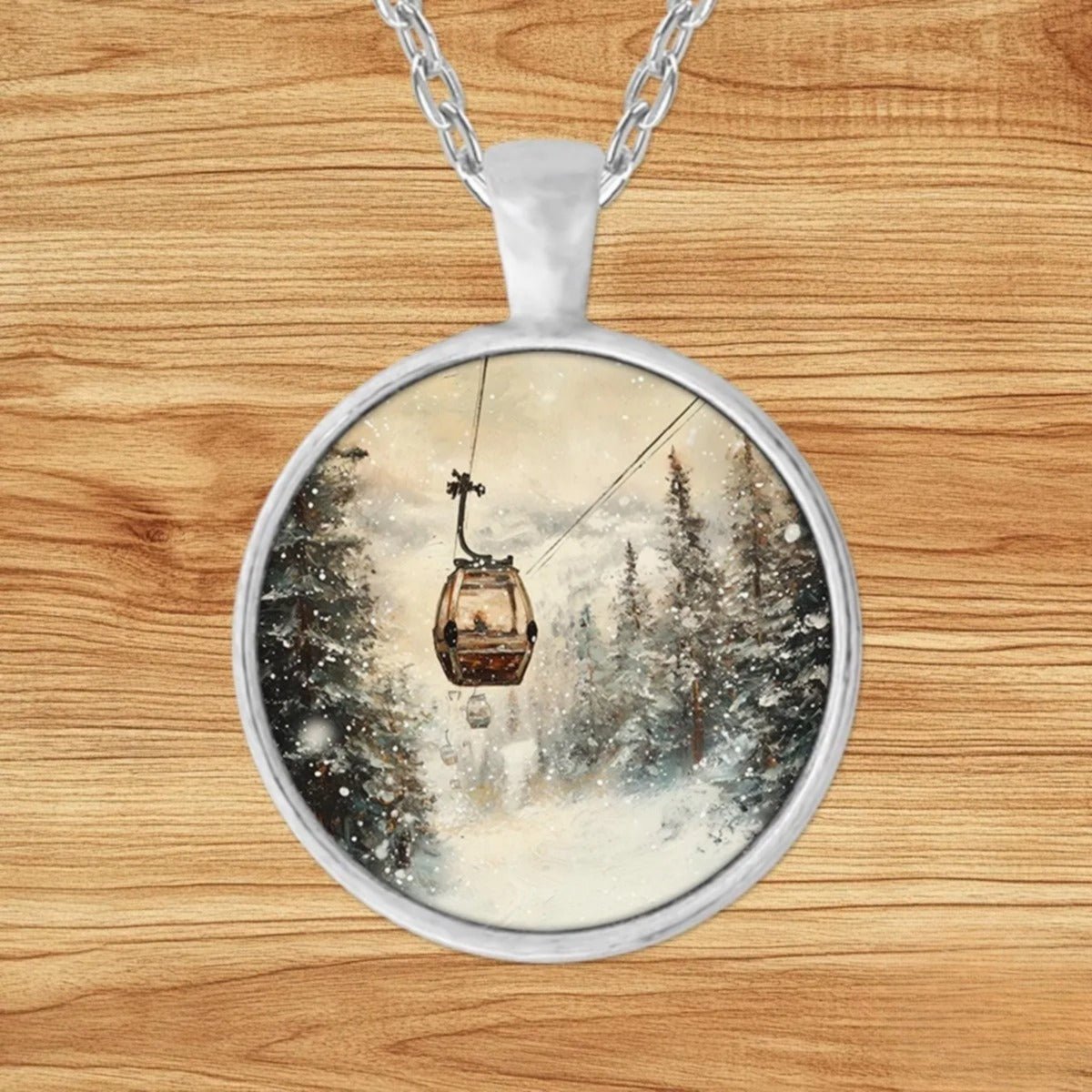 Round silver charm pendant necklace featuring a gondola gliding through snowy alpine peaks with evergreen pines and a warm-toned sky