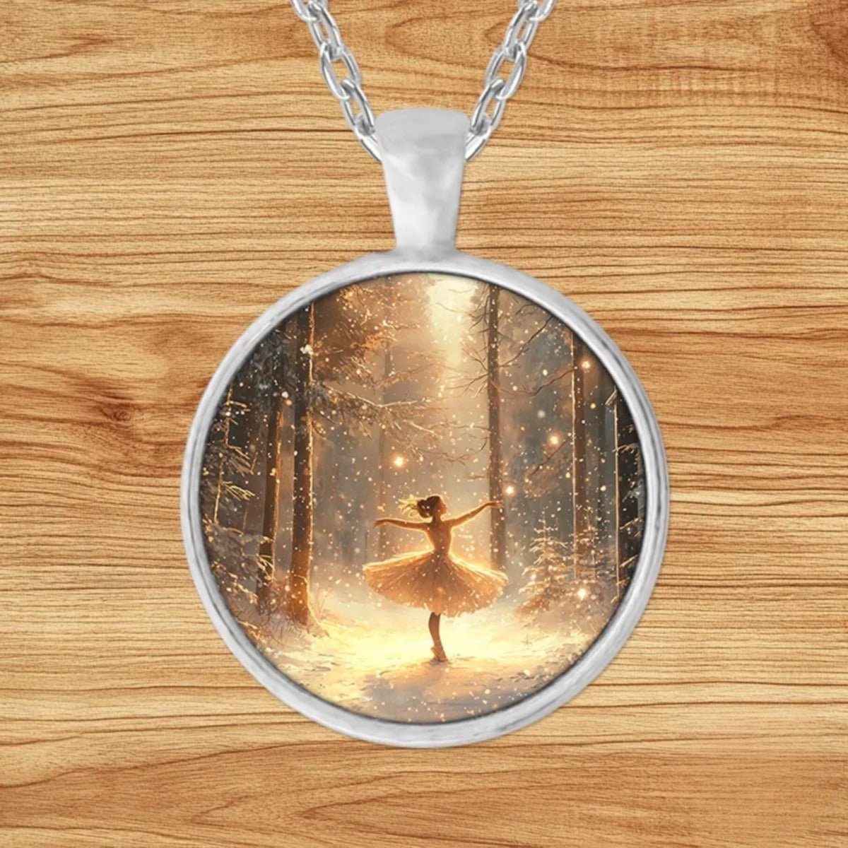 Round silver charm pendant necklace featuring a ballerina mid-pose in a snow-covered forest with golden light and falling snowflakes