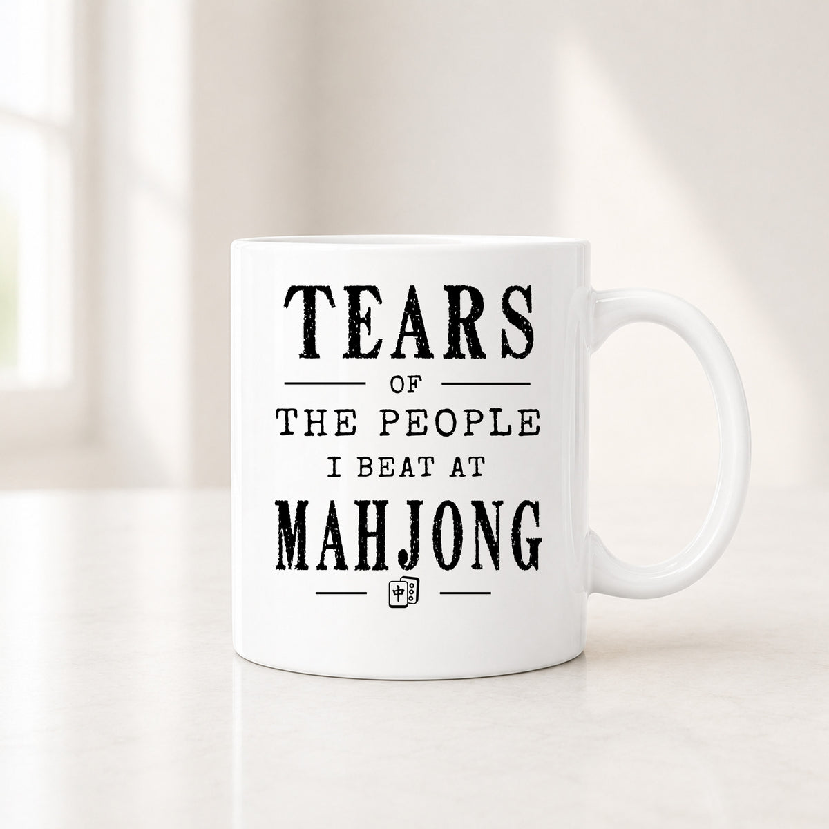 11 oz white Mahjong mug with the black Tears of the People I Beat quote, on a light counter by a window