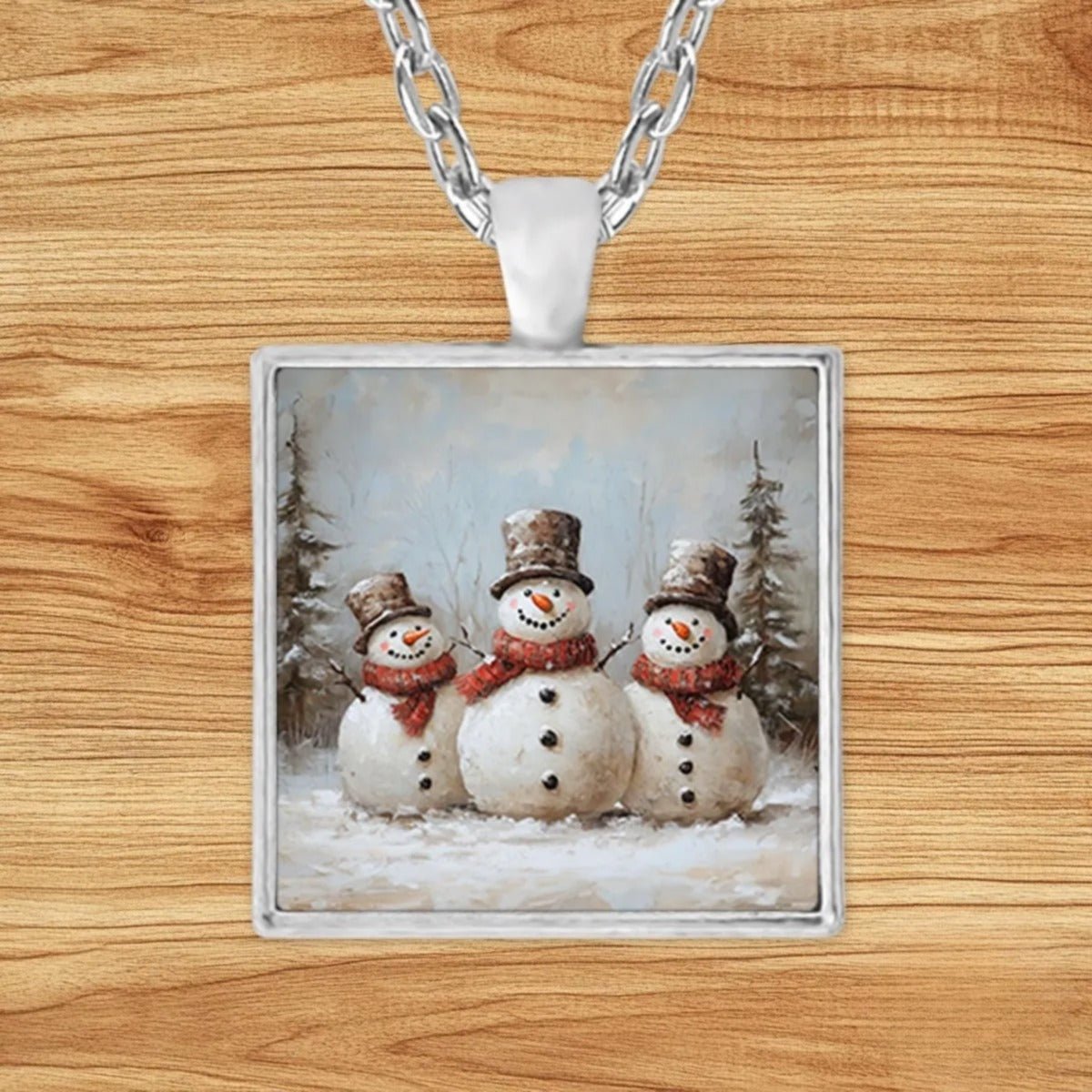 Square silver charm pendant necklace featuring three cheerful snowmen gathered in a snowy pine forest