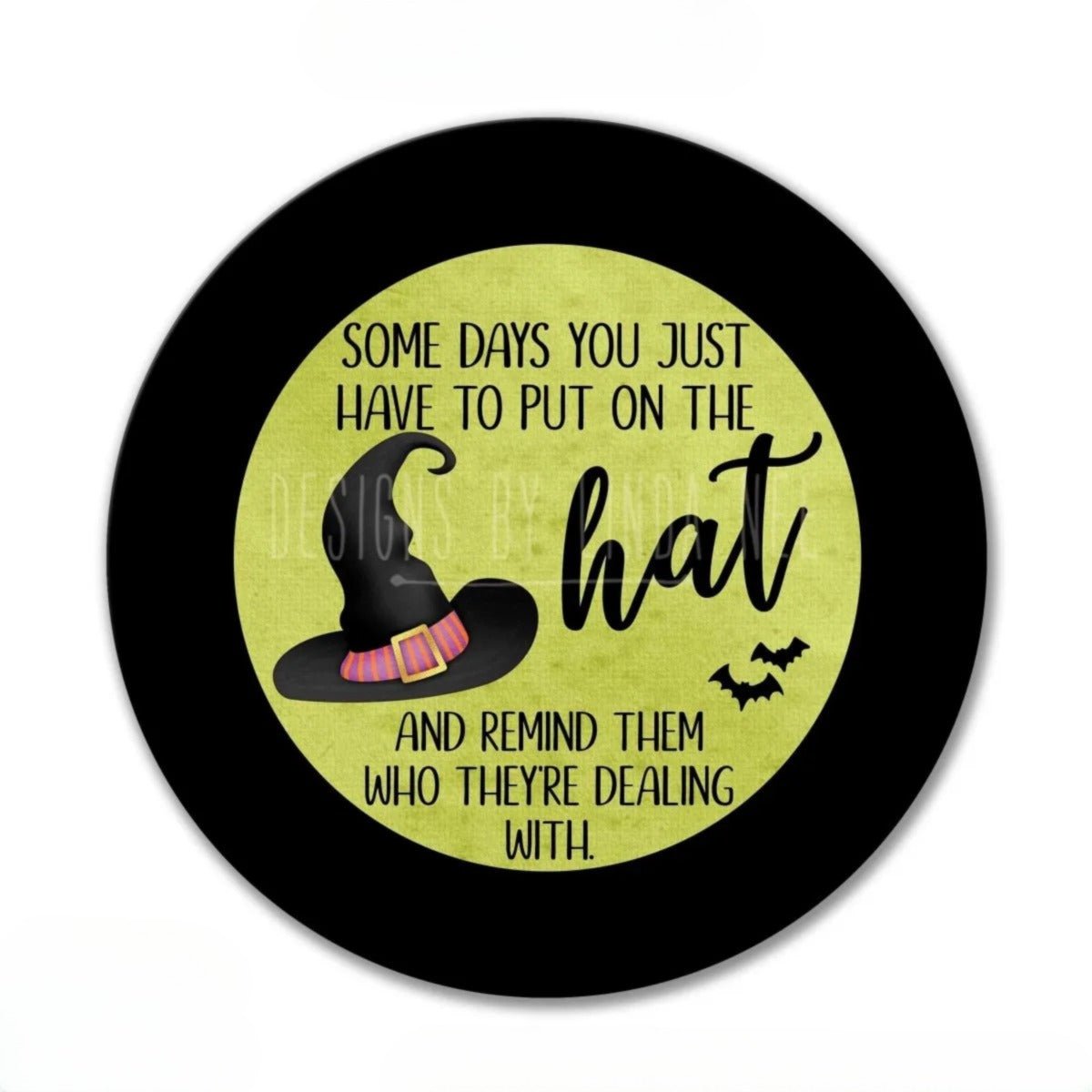 a black circle with a yellow background, containing a stylized illustration of a witch's hat and a humorous text that reads "Some days you just have to put on the hat and remind them who they're dealing with".