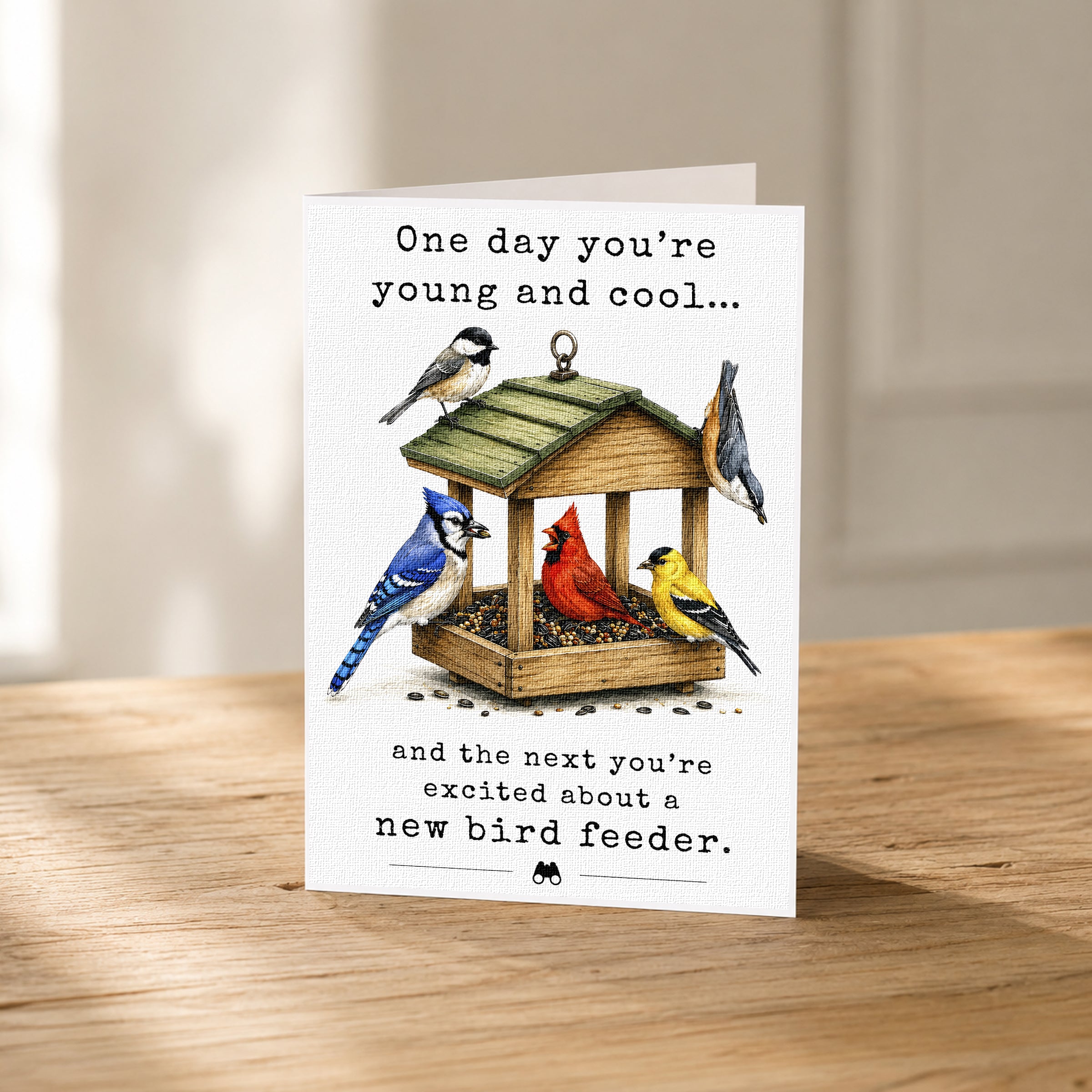 A greeting card with a bird feeder illustration and text that reads "One day you're young and cool... and the next you're excited about a new bird feeder."