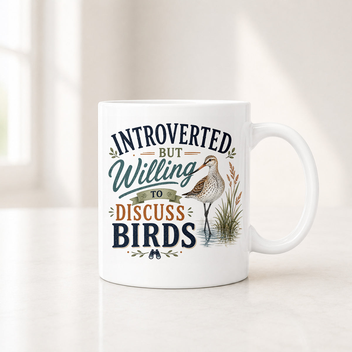 11 oz white shorebird coffee mug with navy, teal and rust lettering beside a long-billed wading bird
