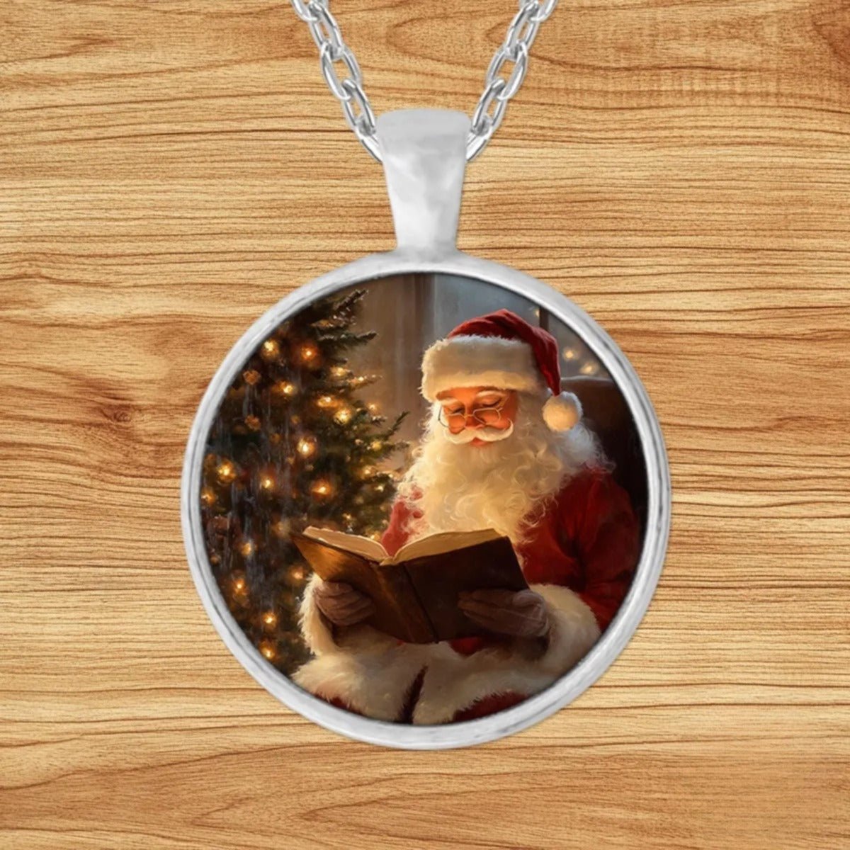 Round silver charm pendant necklace featuring Santa Claus in half-moon glasses reading a leather-bound book beside a glowing Christmas tree