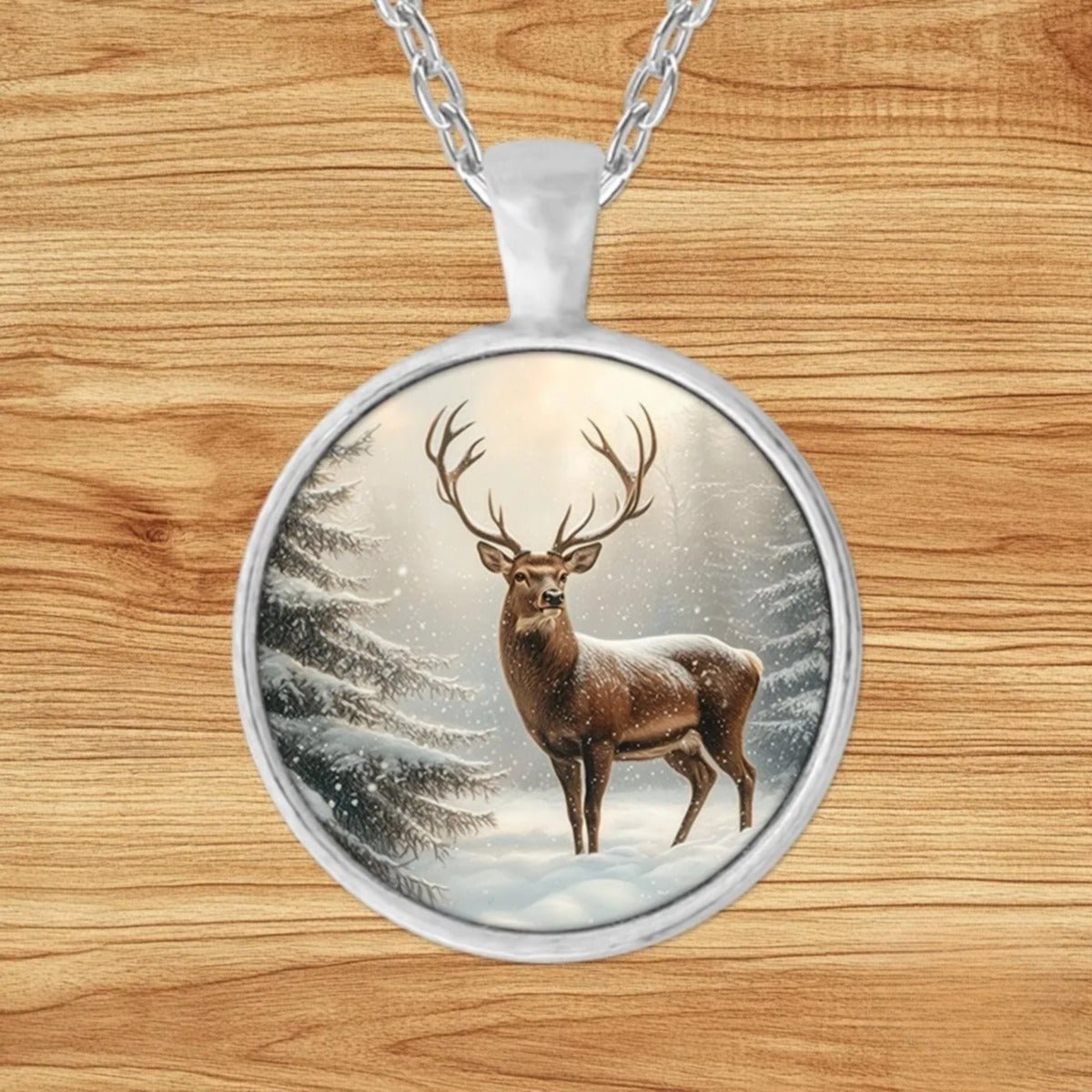 Round silver charm pendant necklace featuring a brown deer standing among towering snow-covered pines in soft winter light