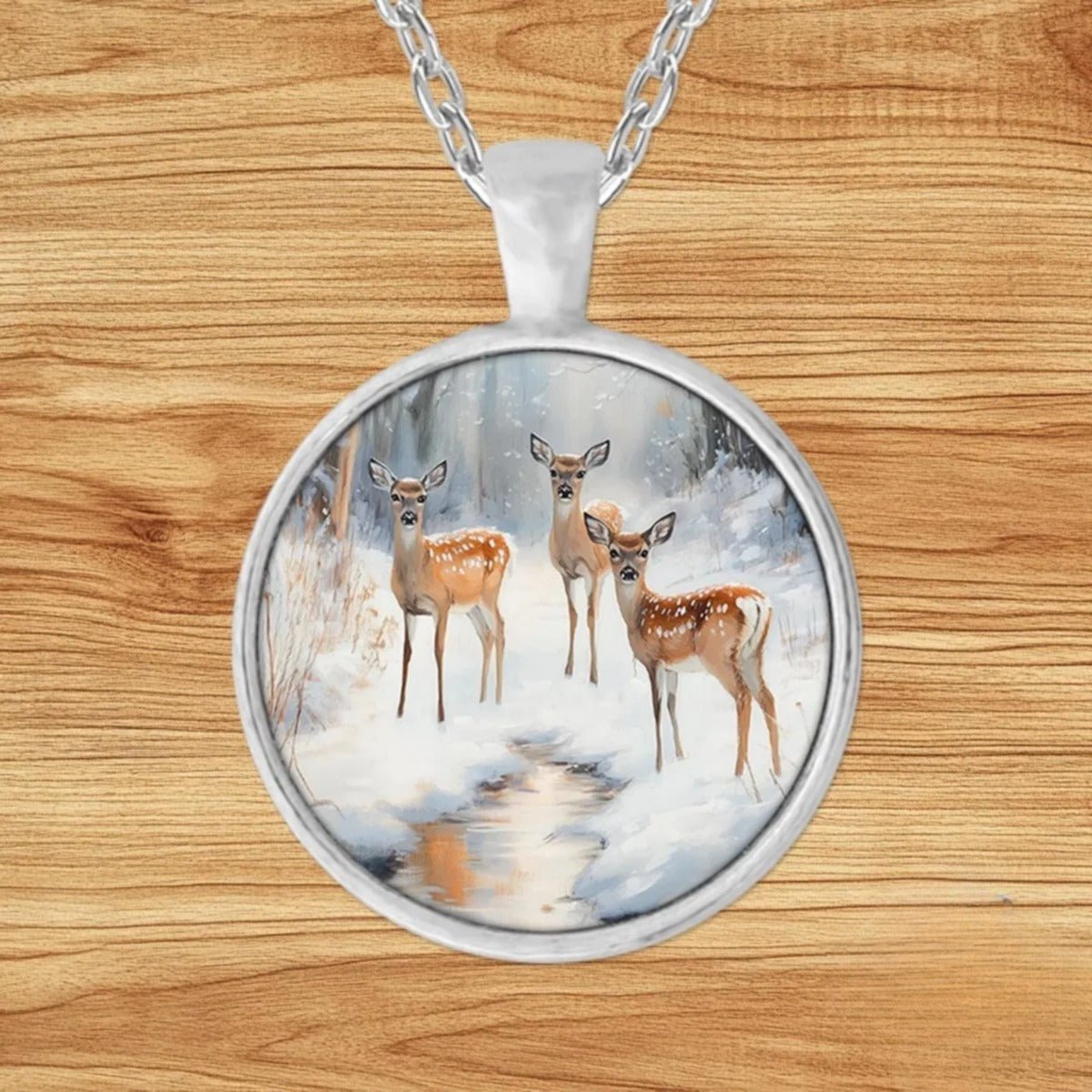 Round silver charm pendant necklace featuring three young spotted fawns gathered beside a snowy forest stream