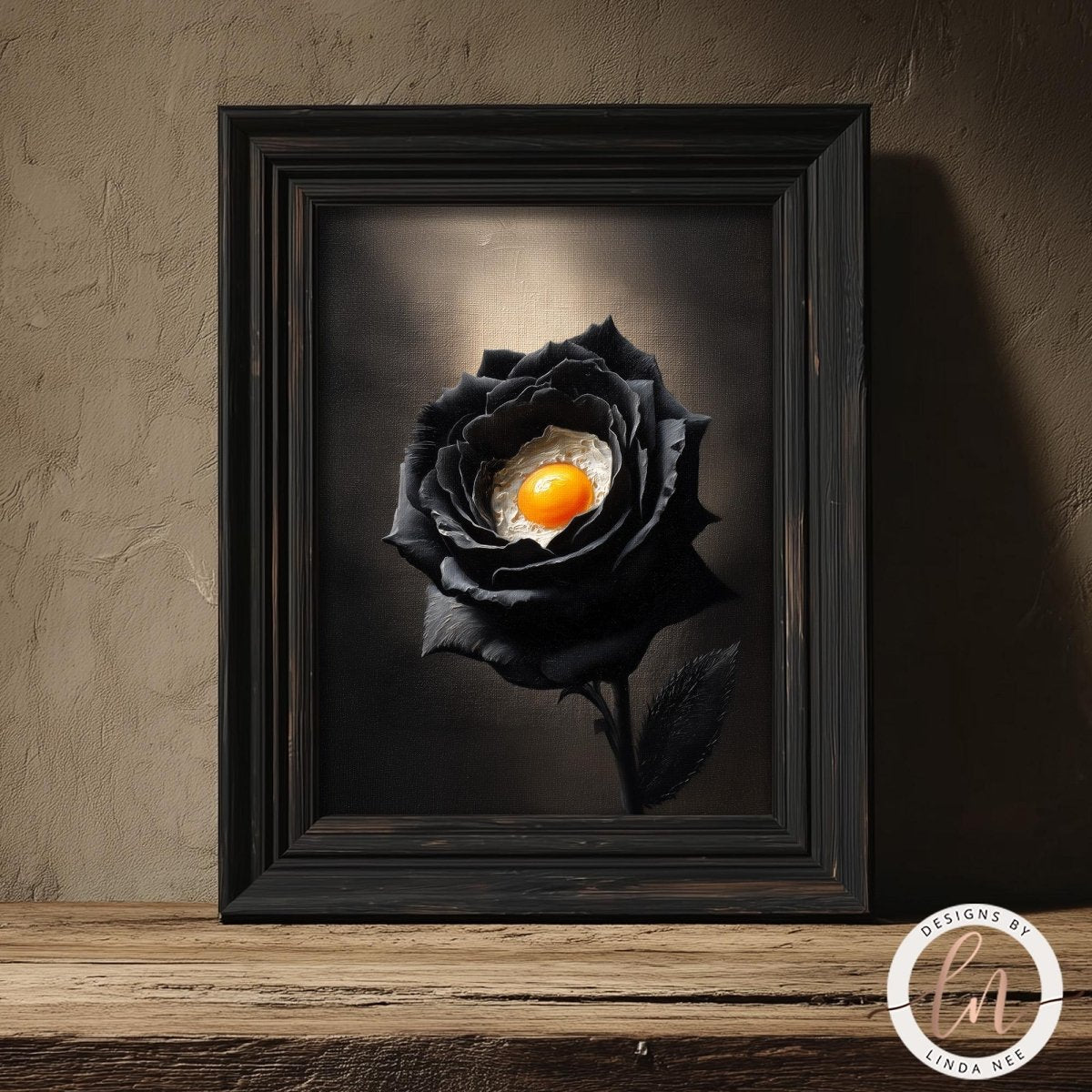 A framed image of a black rose with an orange center, placed on a wooden surface against a textured wall.