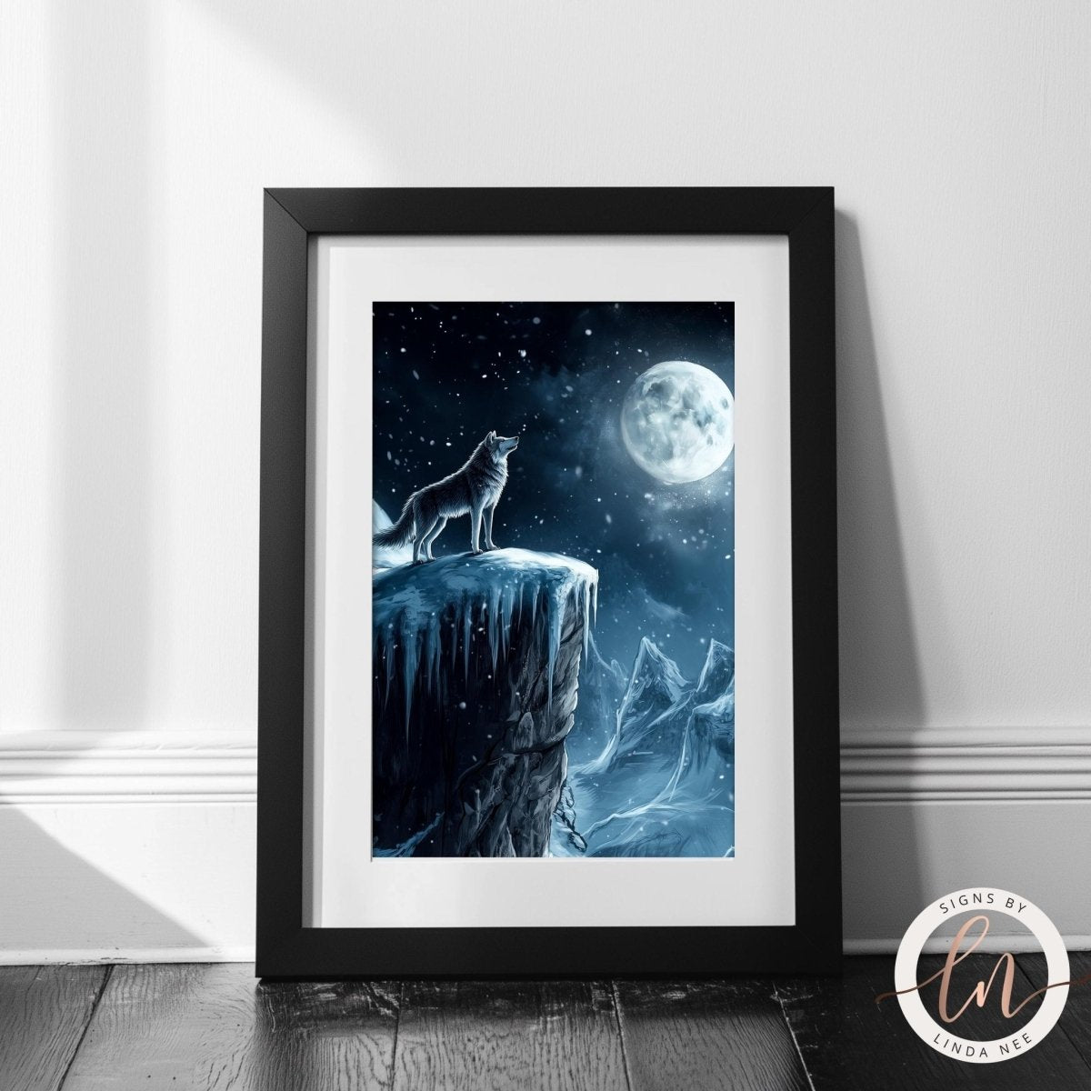 A framed artwork depicting a wolf standing on a cliff, gazing out at a full moon and a snowy mountain landscape.