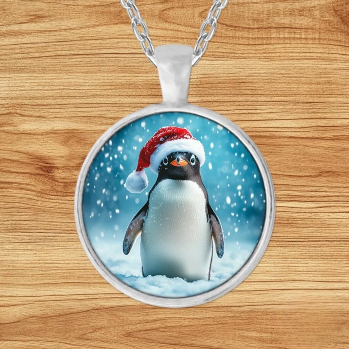 Round silver charm pendant necklace featuring a cheerful penguin in a bright red Santa hat amid swirling snowflakes
