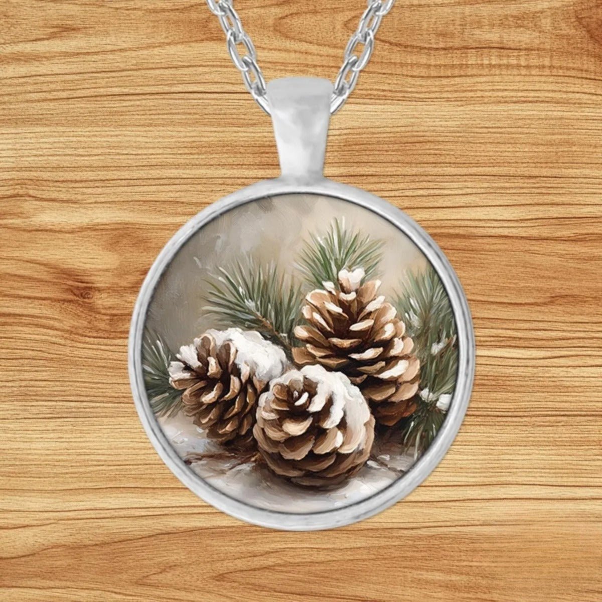Round silver charm pendant necklace featuring three snow-dusted pinecones nestled among green pine sprigs