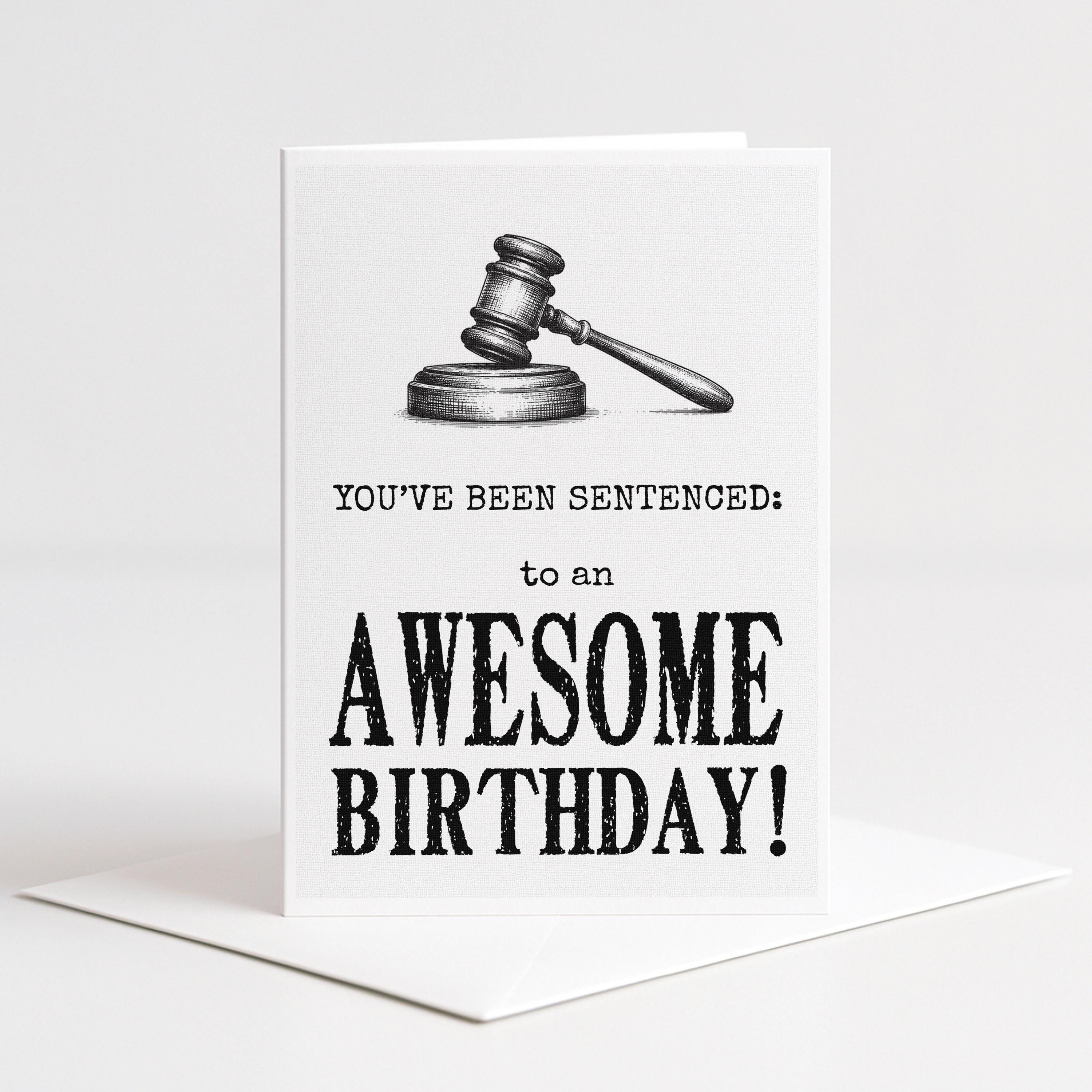 White 5-by-7 greeting card displayed upright on a white envelope with a detailed black gavel illustration and distressed typography reading, “You’ve been sentenced to an awesome birthday!”