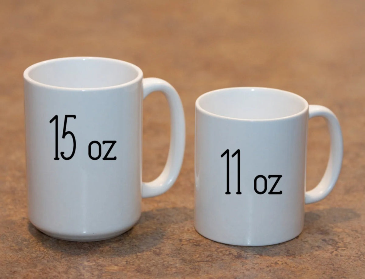 Size comparison of the 11 oz and 15 oz white ceramic mugs standing side by side on a wooden counter
