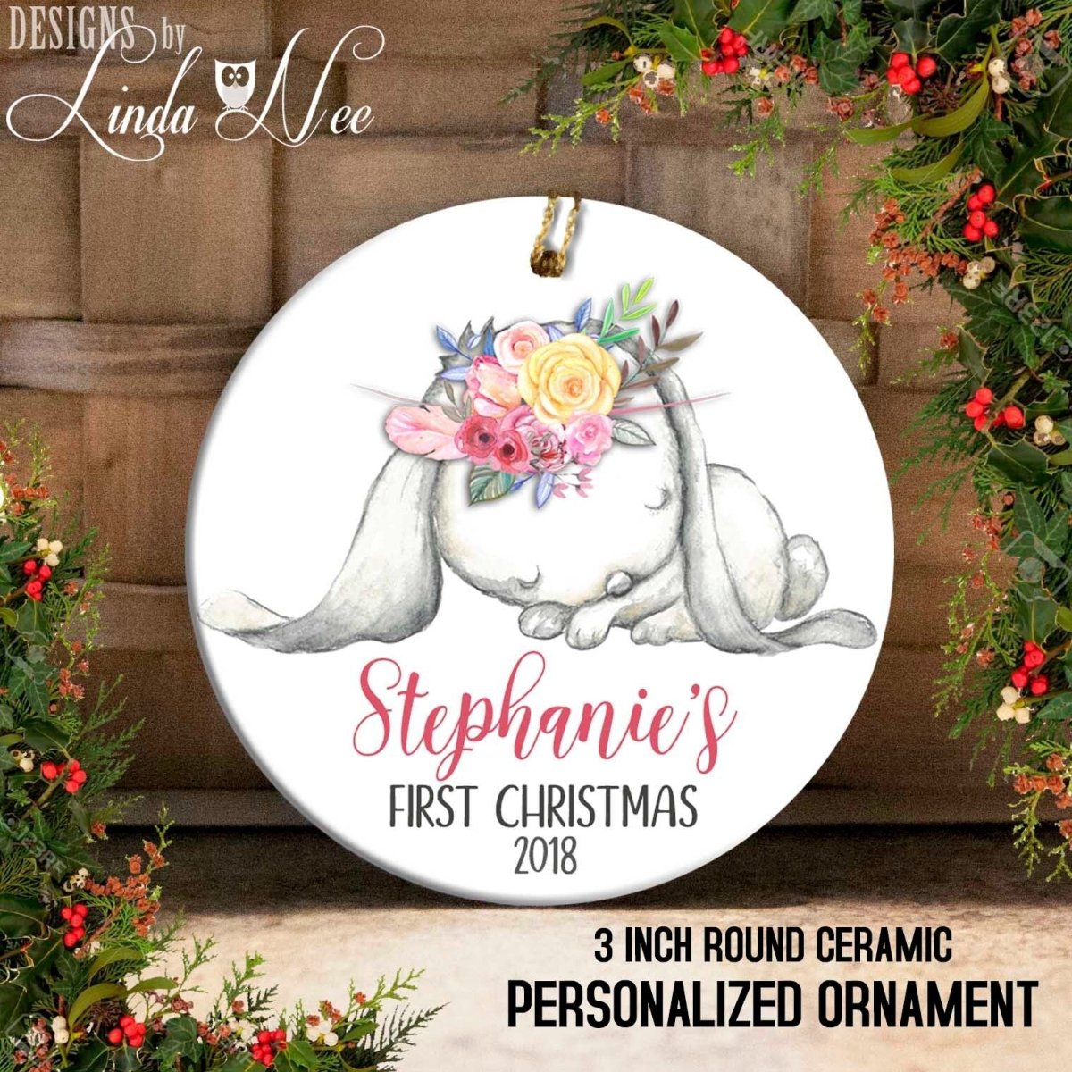 A round ceramic ornament with a white rabbit and colorful flowers, labeled as "Stephanie's First Christmas 2018" and "3 inch round ceramic personalized ornament".