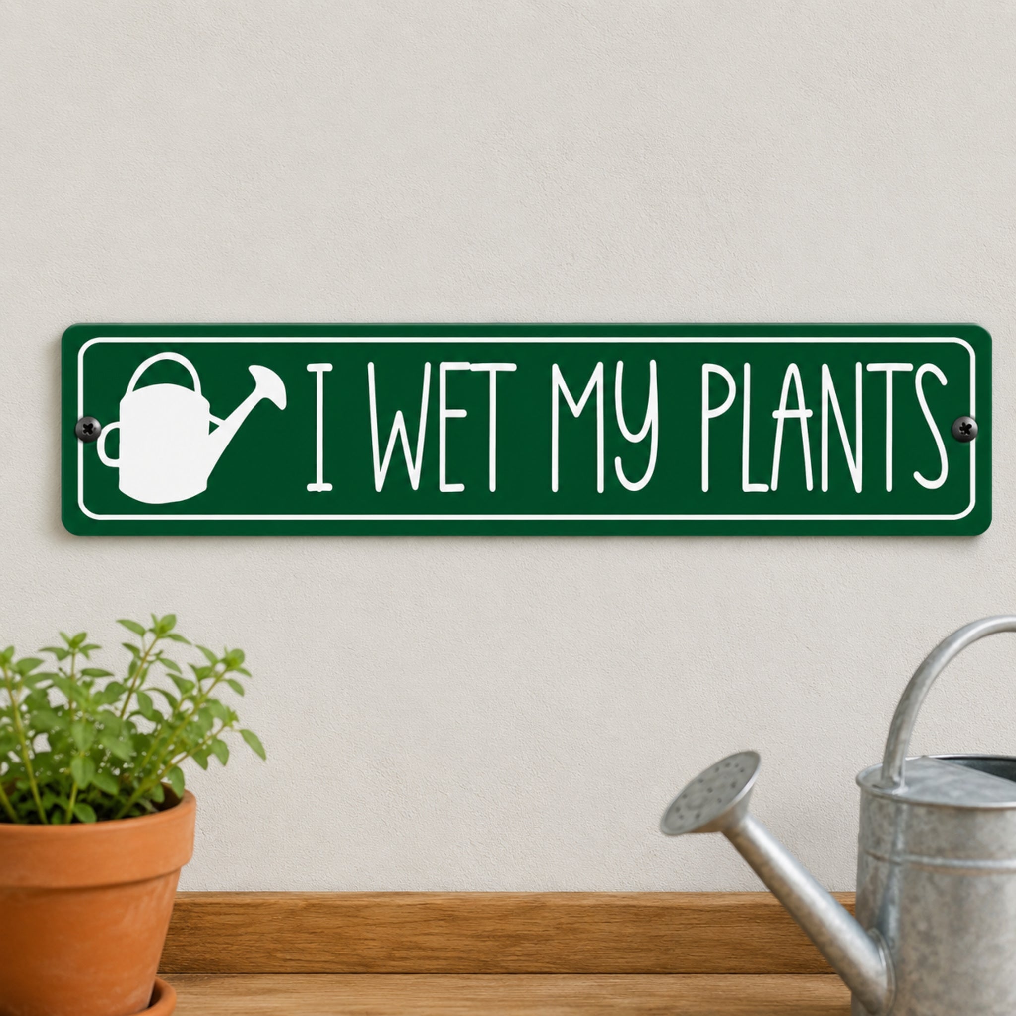 a green rectangular sign with the text "I WET MY PLANTS" on it, along with a white watering can icon. The sign is mounted on a wall, and there is a potted plant to the left of the sign.