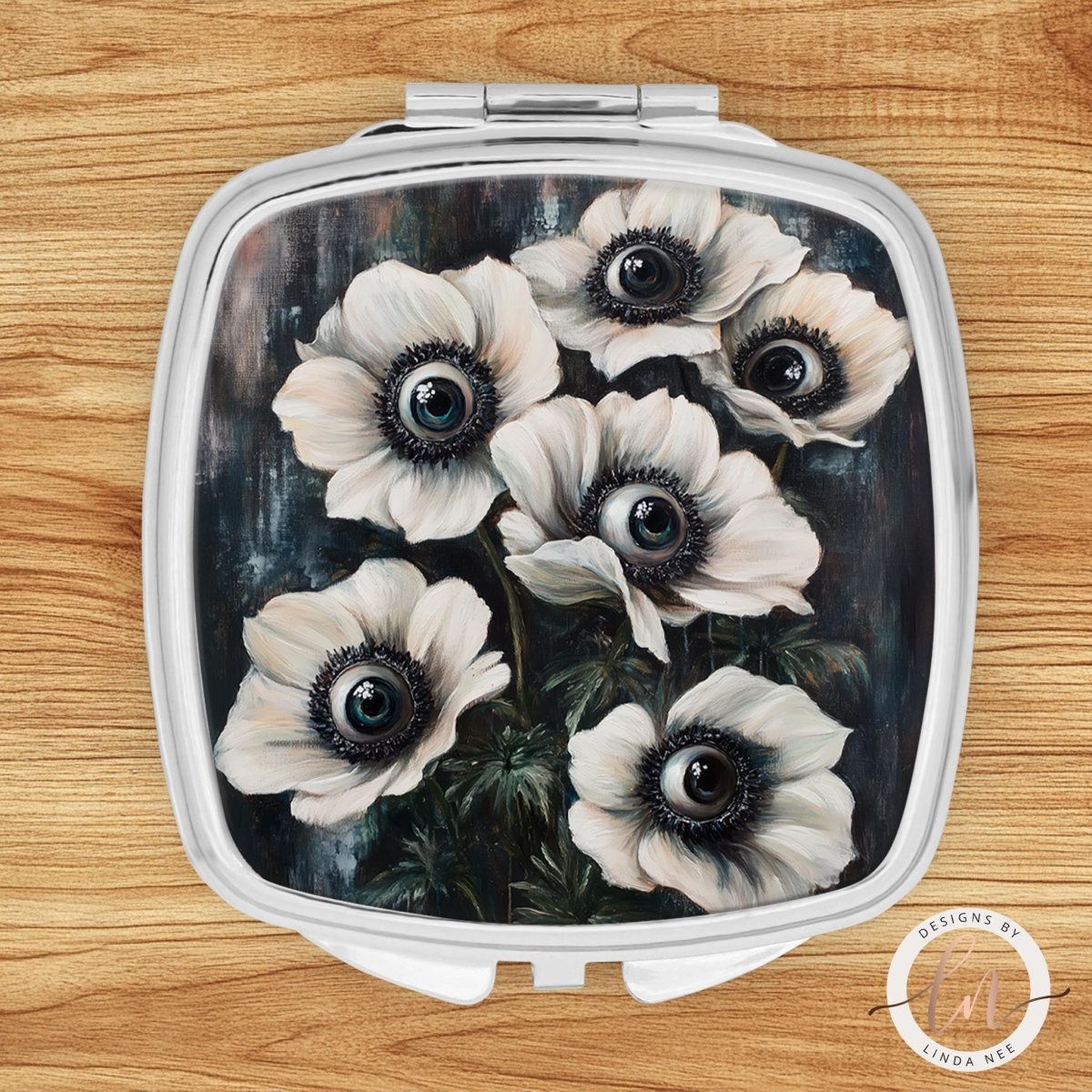 A compact mirror with a floral design featuring white flowers with black centers.