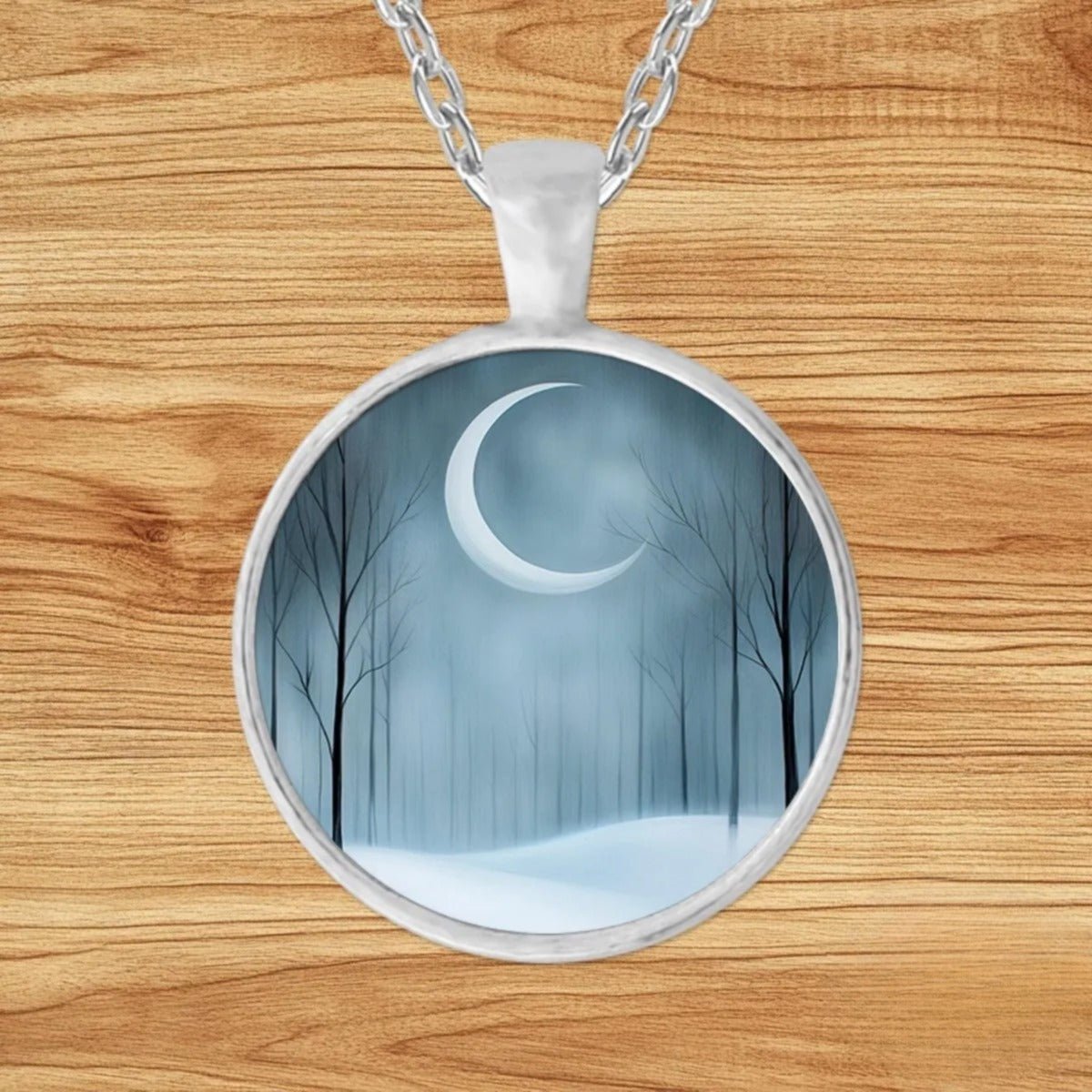 Round silver charm pendant necklace featuring a glowing crescent moon over a misty, snow-covered forest