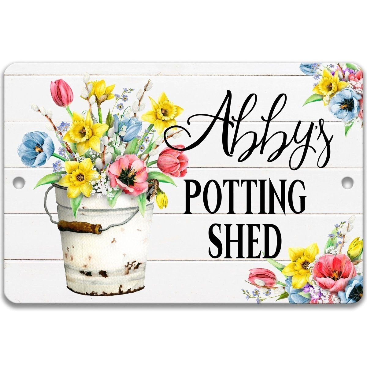 A white wooden sign with a bucket filled with colorful flowers, including tulips, daffodils, and other spring flowers, along with the text "Abby's POTTING SHED".