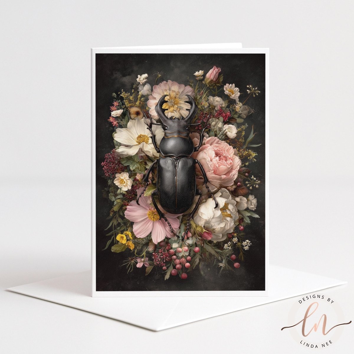 A 5x7 linen-textured greeting card featuring a majestic black stag beetle surrounded by a vintage-style floral arrangement in shades of cream and dusty rose. The card is displayed next to a premium white envelope on a neutral surface, showcasing a gothic botanical aesthetic.
