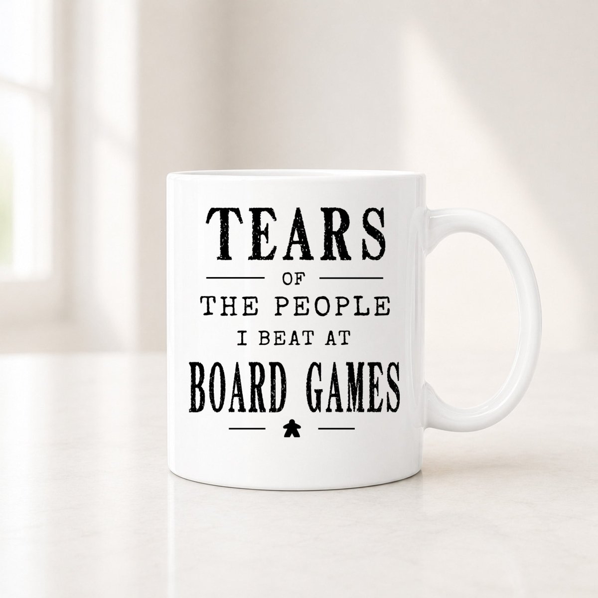 11 oz white board games mug with the black Tears of the People I Beat quote, on a light counter by a window