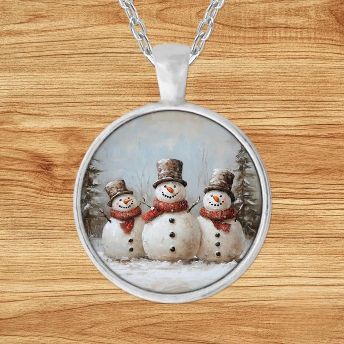 Round silver charm pendant necklace featuring three cheerful snowmen gathered in a snowy pine forest