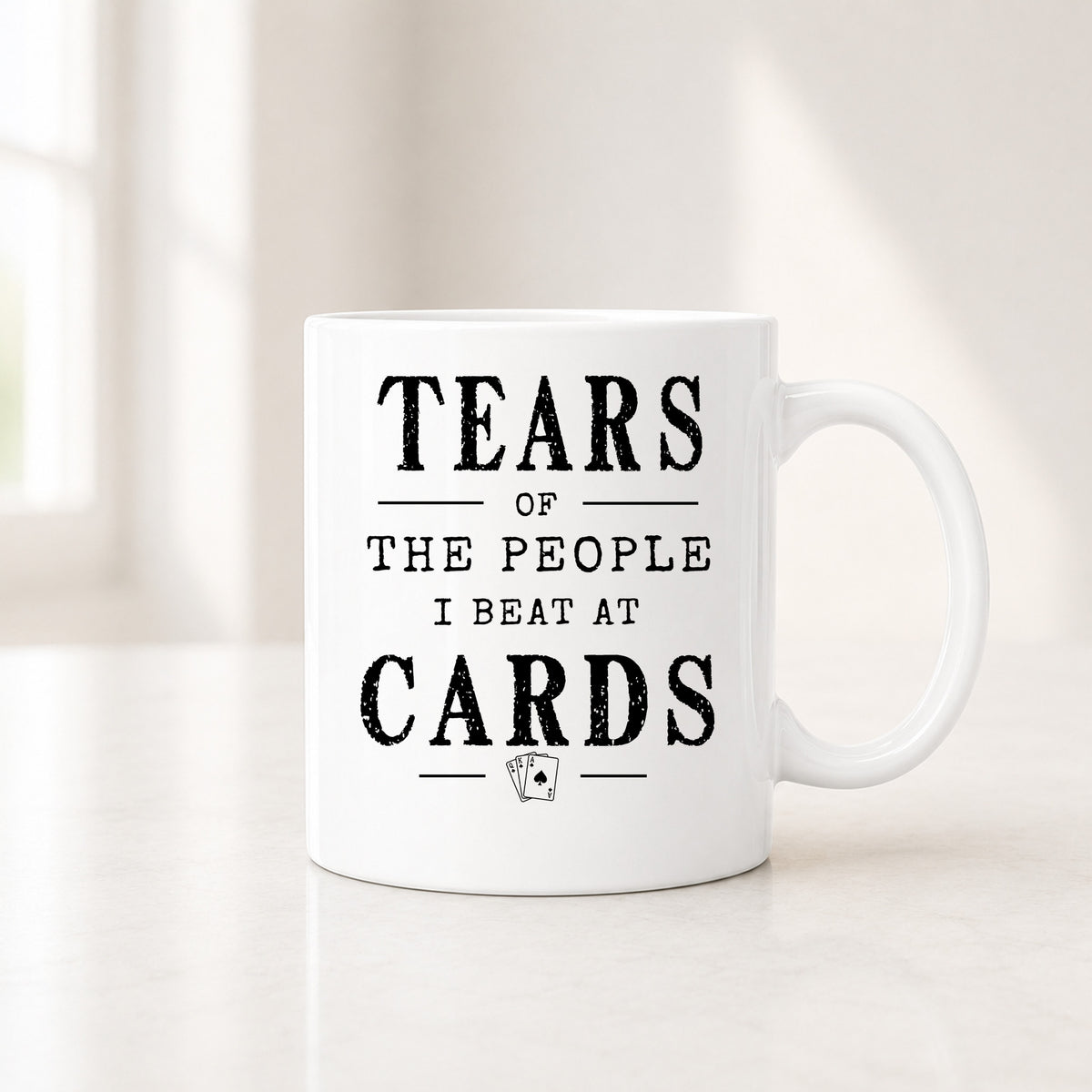 11 oz white cards mug with the black Tears of the People I Beat quote, on a light counter by a window