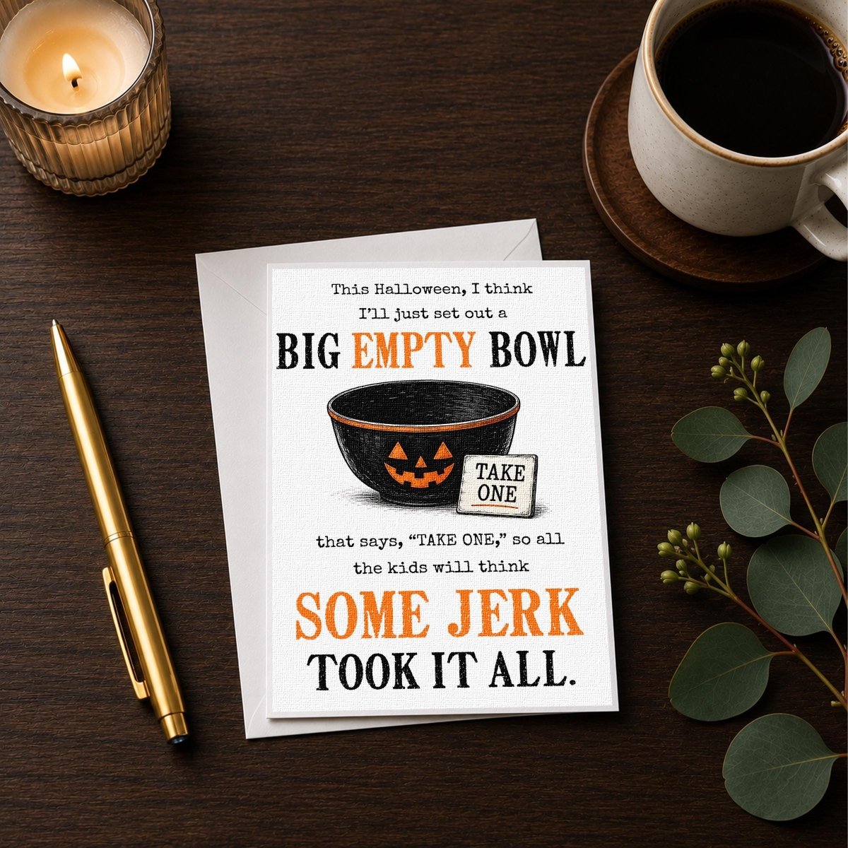 a Halloween-themed card with a pumpkin bowl and a humorous message, accompanied by a candle, a pen, and a cup of coffee on a wooden surface.