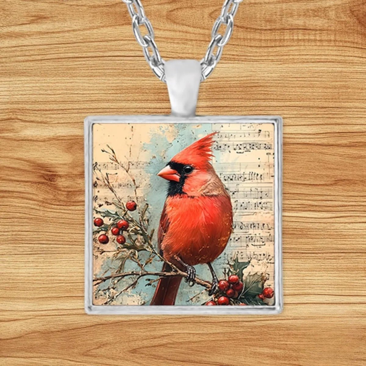Square silver charm pendant necklace featuring a vivid red cardinal perched on a holly branch over vintage sheet music