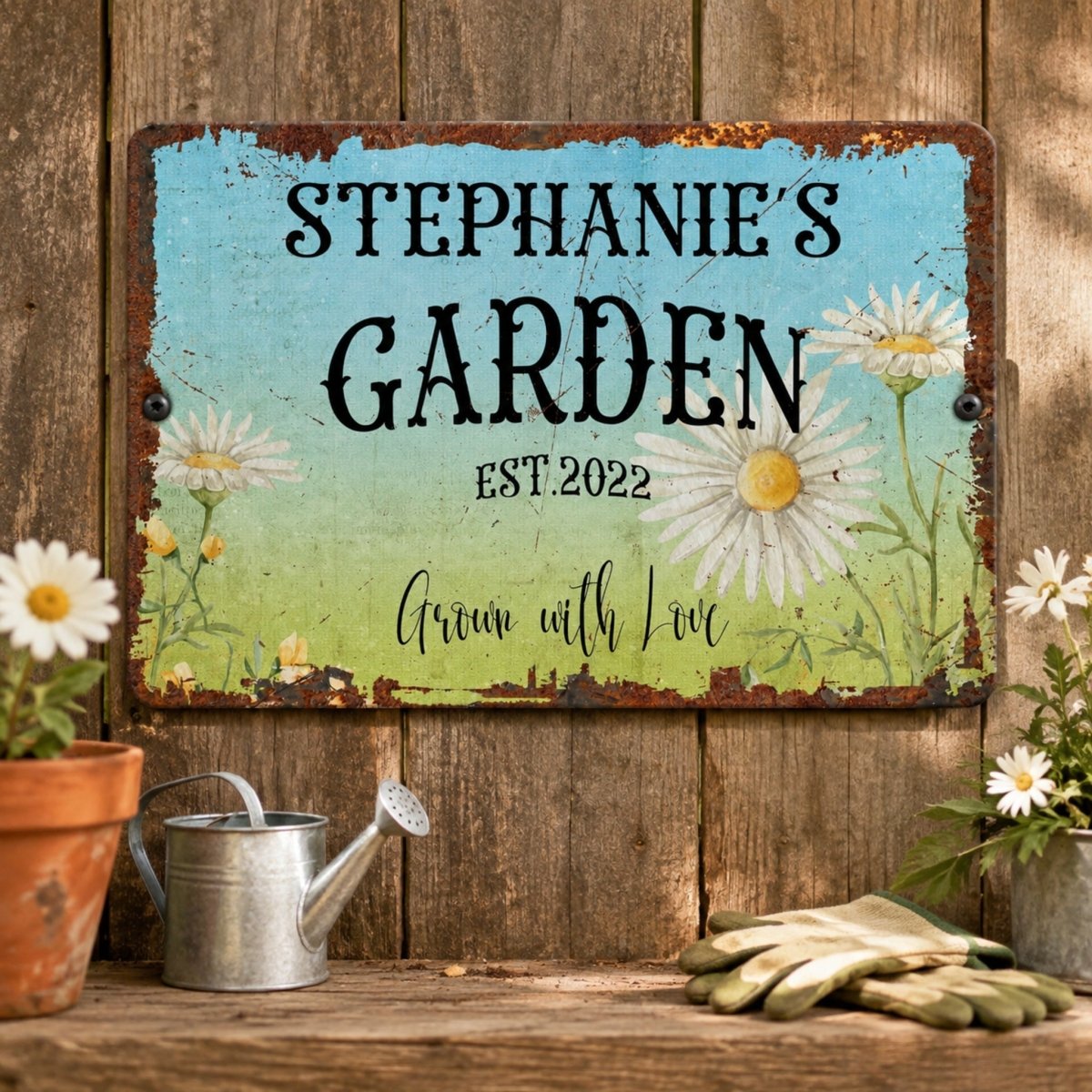 a rustic garden sign with a blue background and white flowers, hanging on a wooden wall. The sign reads "Stephanie's Garden" and "Est.2022", indicating the name and establishment year of the garden. In the foreground, there are potted plants and gardening tools, suggesting a well-maintained and organized garden space.