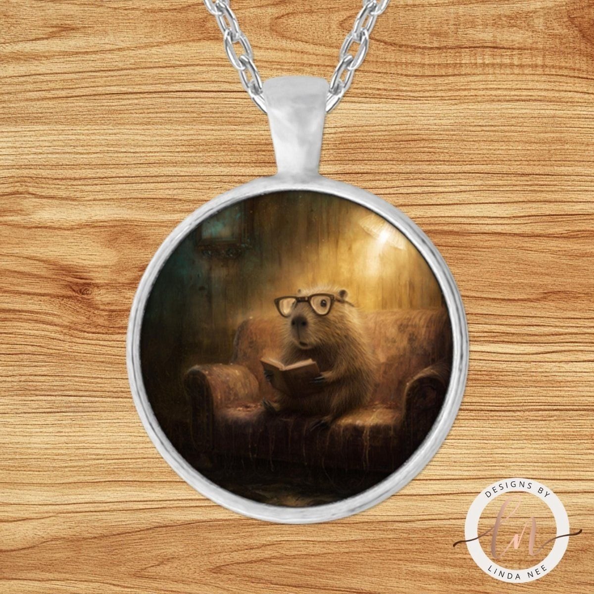 A pendant necklace with a circular design featuring a capybara wearing glasses and reading a book.