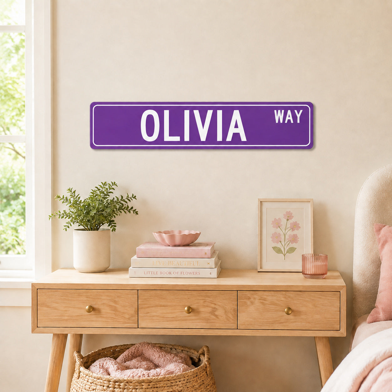 a bedroom setting with a purple street sign that reads "OLIVIA WAY" mounted on the wall above a wooden dresser. The dresser has various items on it, including a plant, books, and a framed picture.