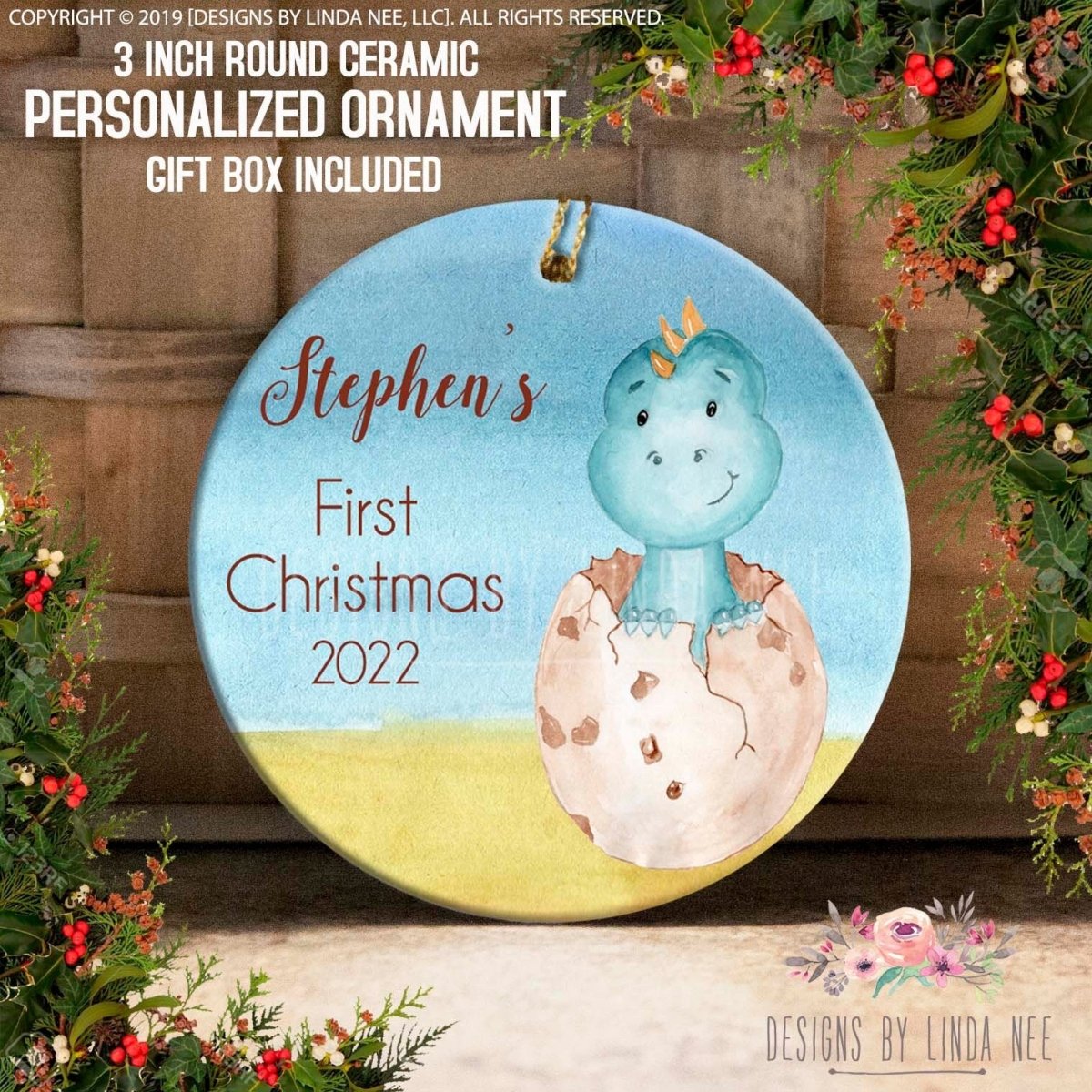 The image is a ceramic ornament featuring a blue dinosaur in a cracked egg, surrounded by holiday decorations such as berries and greenery. The ornament is personalized for "Stephan's First Christmas 2020".