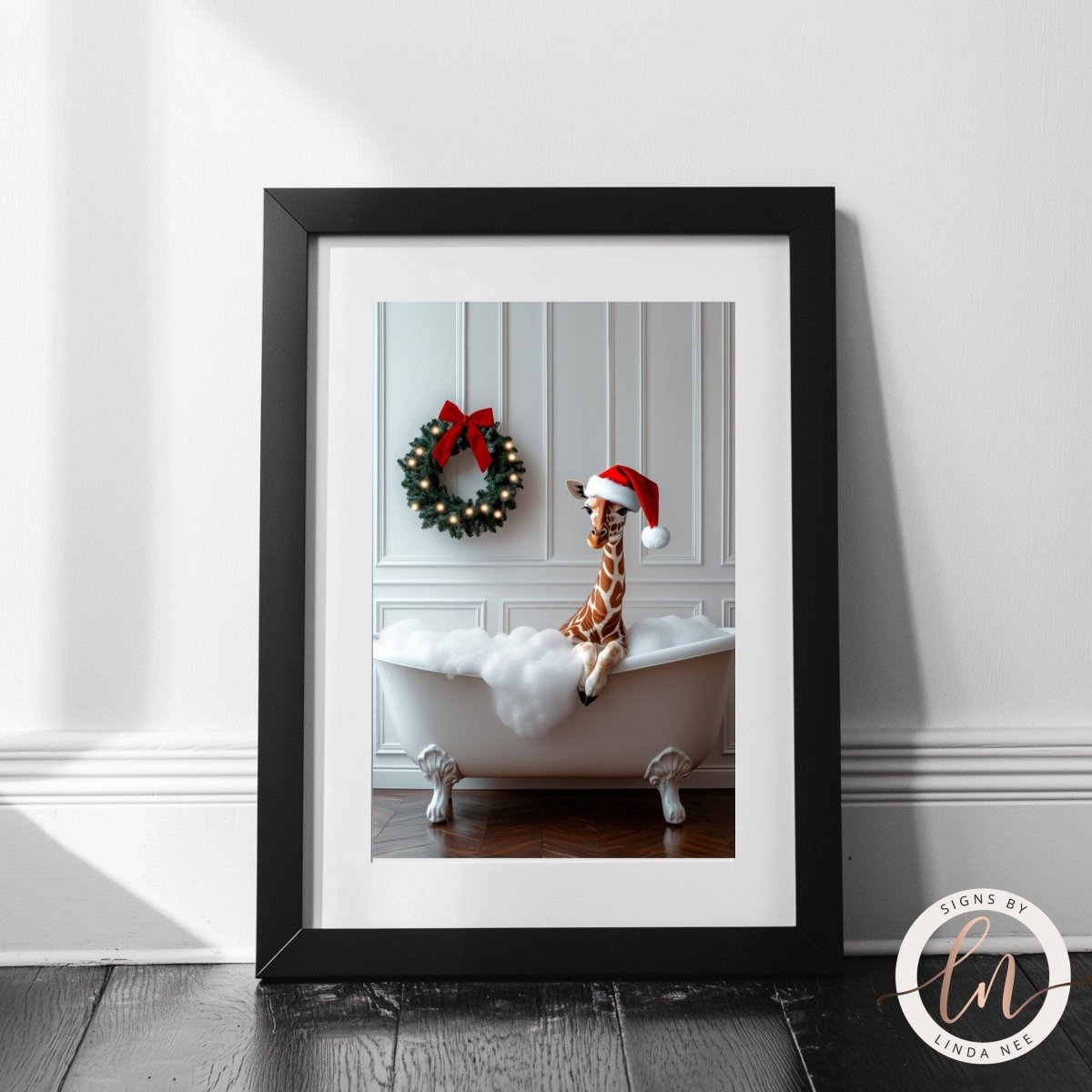 A framed photograph of a giraffe sitting in a bathtub, wearing a Santa hat, with a wreath hanging on the wall behind it.