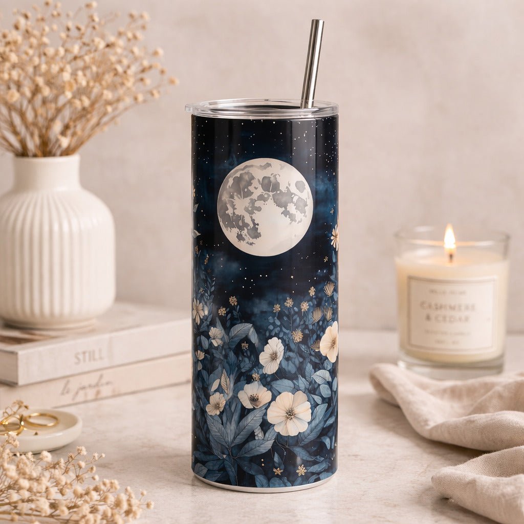 a tall, cylindrical tumbler with a floral design on it, placed on a table next to a lit candle and some books.