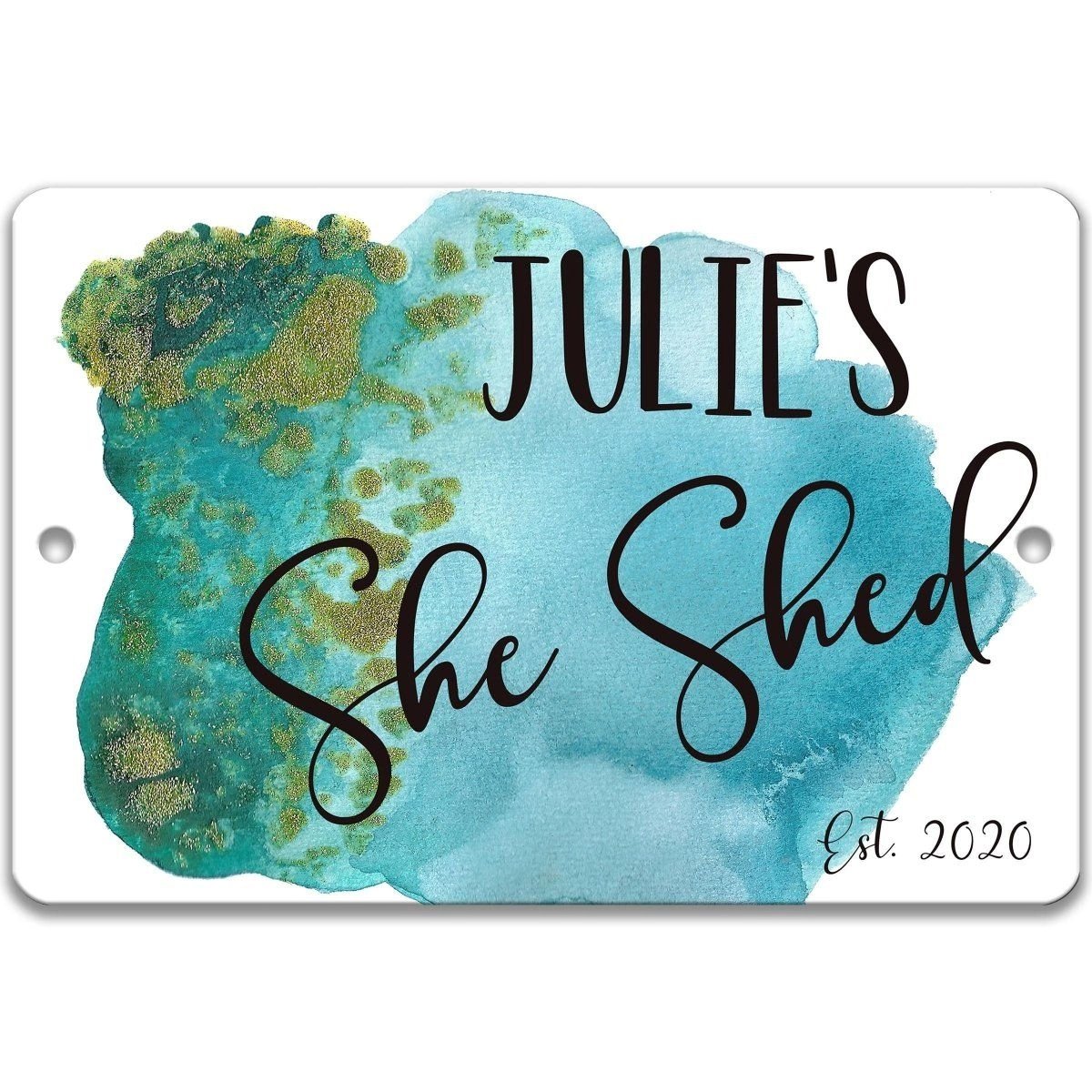 A sign with the text "JULIE'S She Shed" written in cursive font, with a watercolor-like background in shades of blue and green.